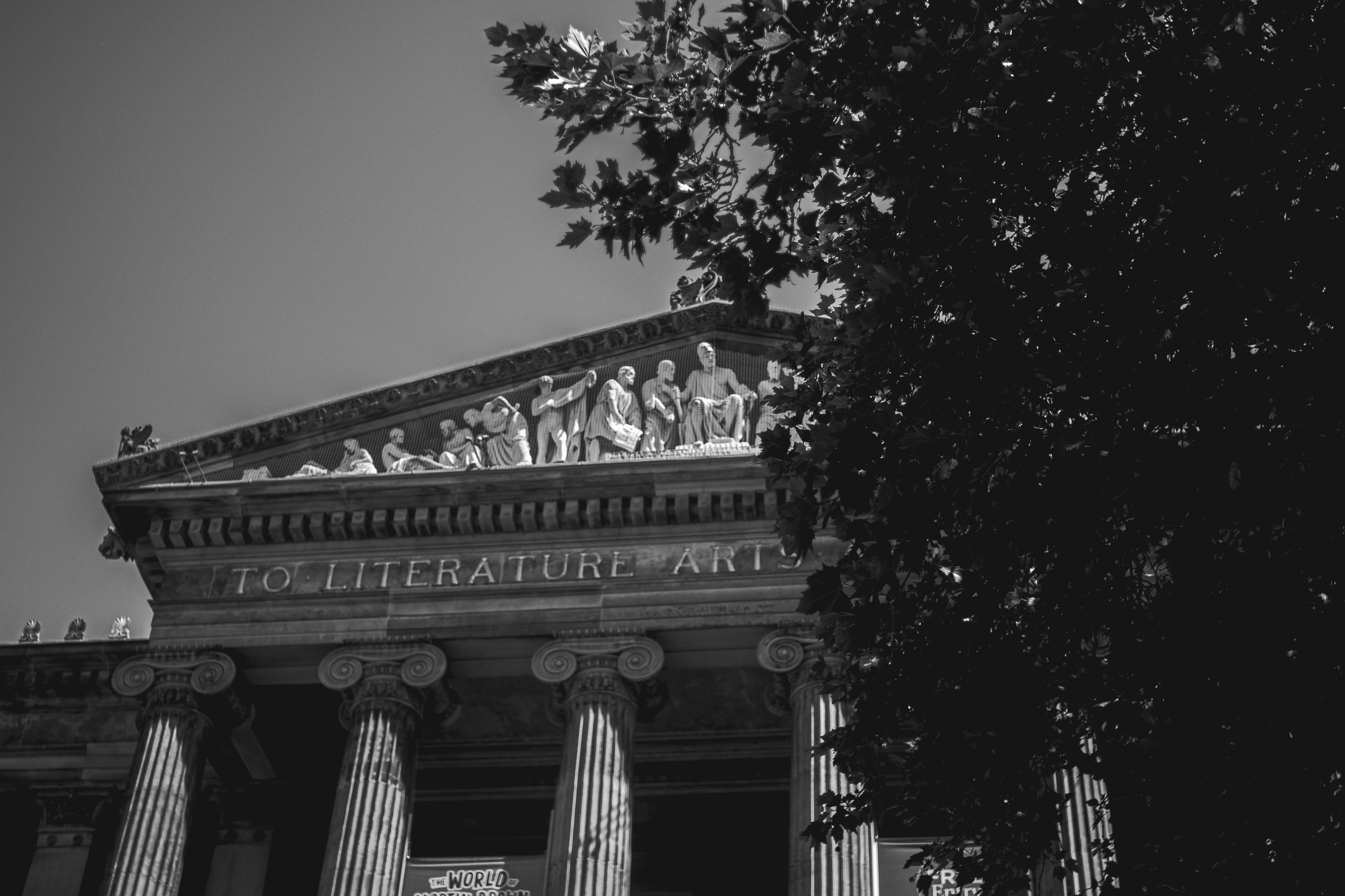 Ornate classical building facade with sculptures and tree in foreground.