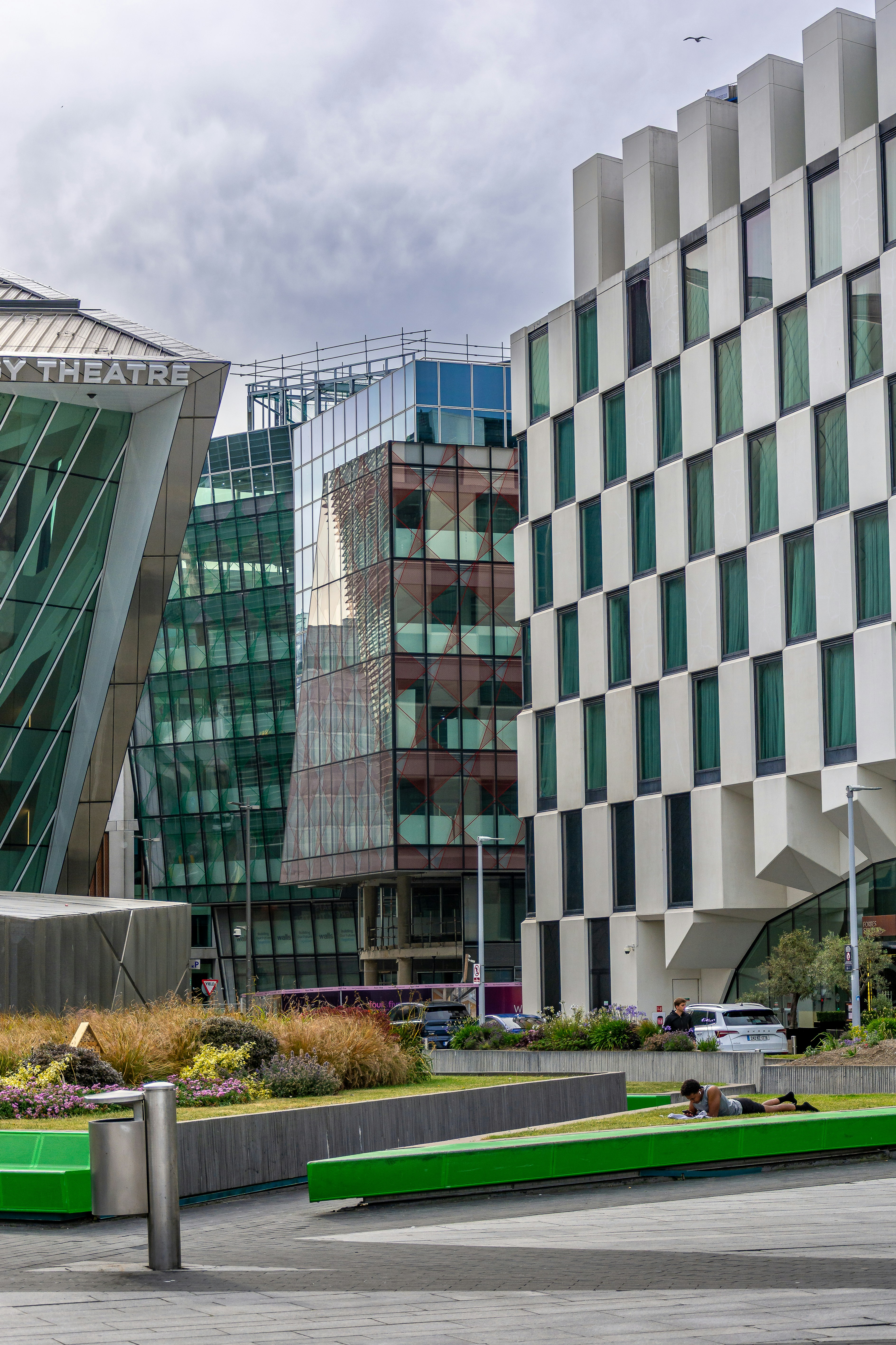 Diverse modern buildings overlook a green park with a person.