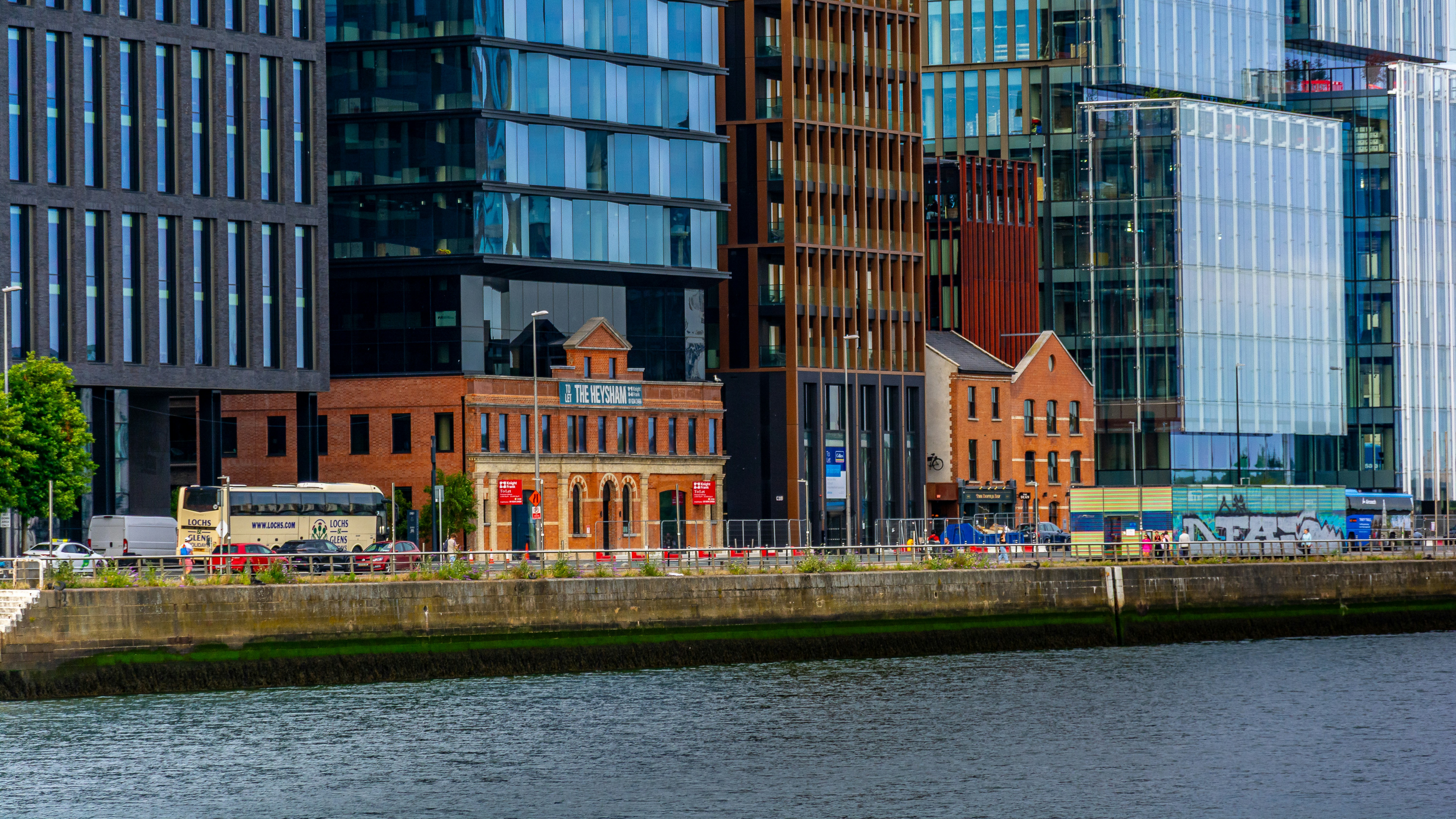 Modern and old buildings line a city riverfront.