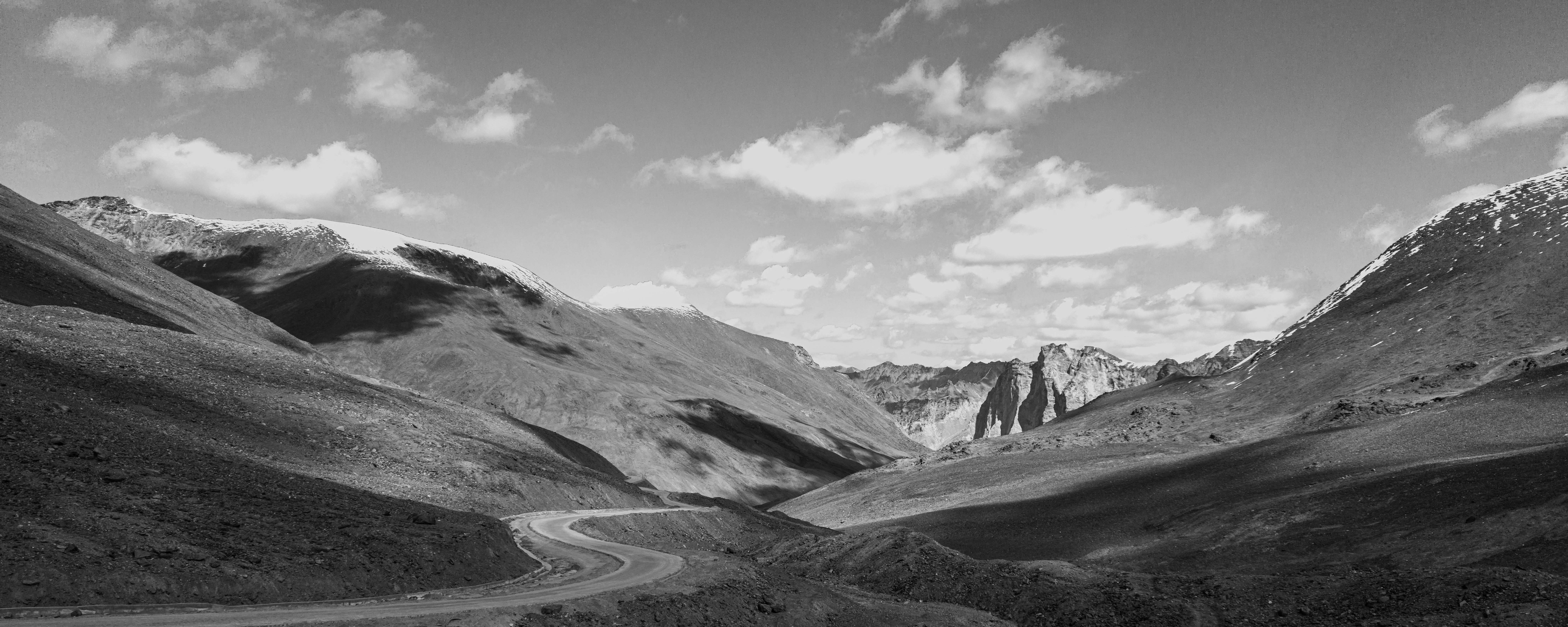 Winding road through a majestic mountain landscape under cloudy sky.