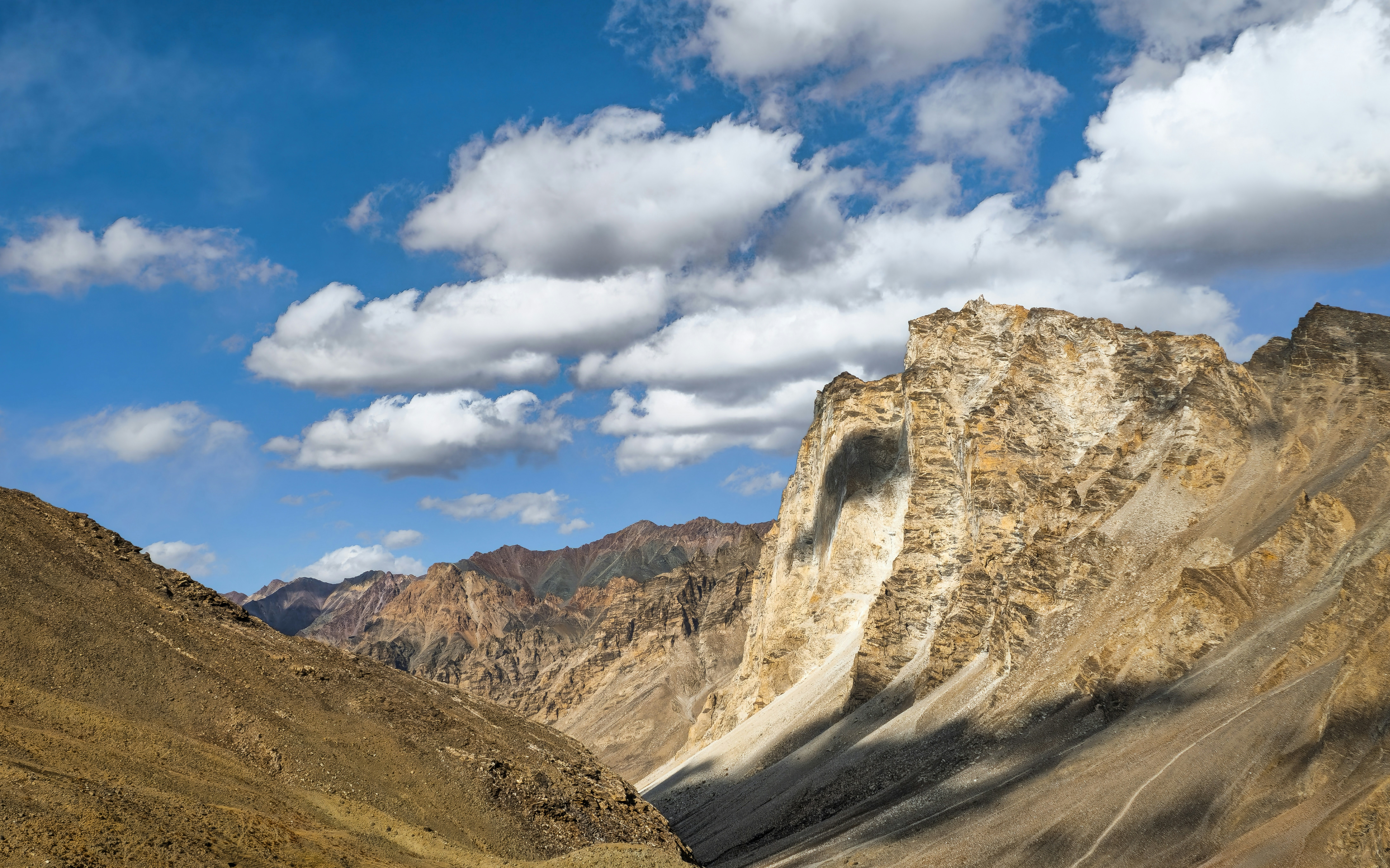 Arid mountain landscape under a blue sky with white clouds.