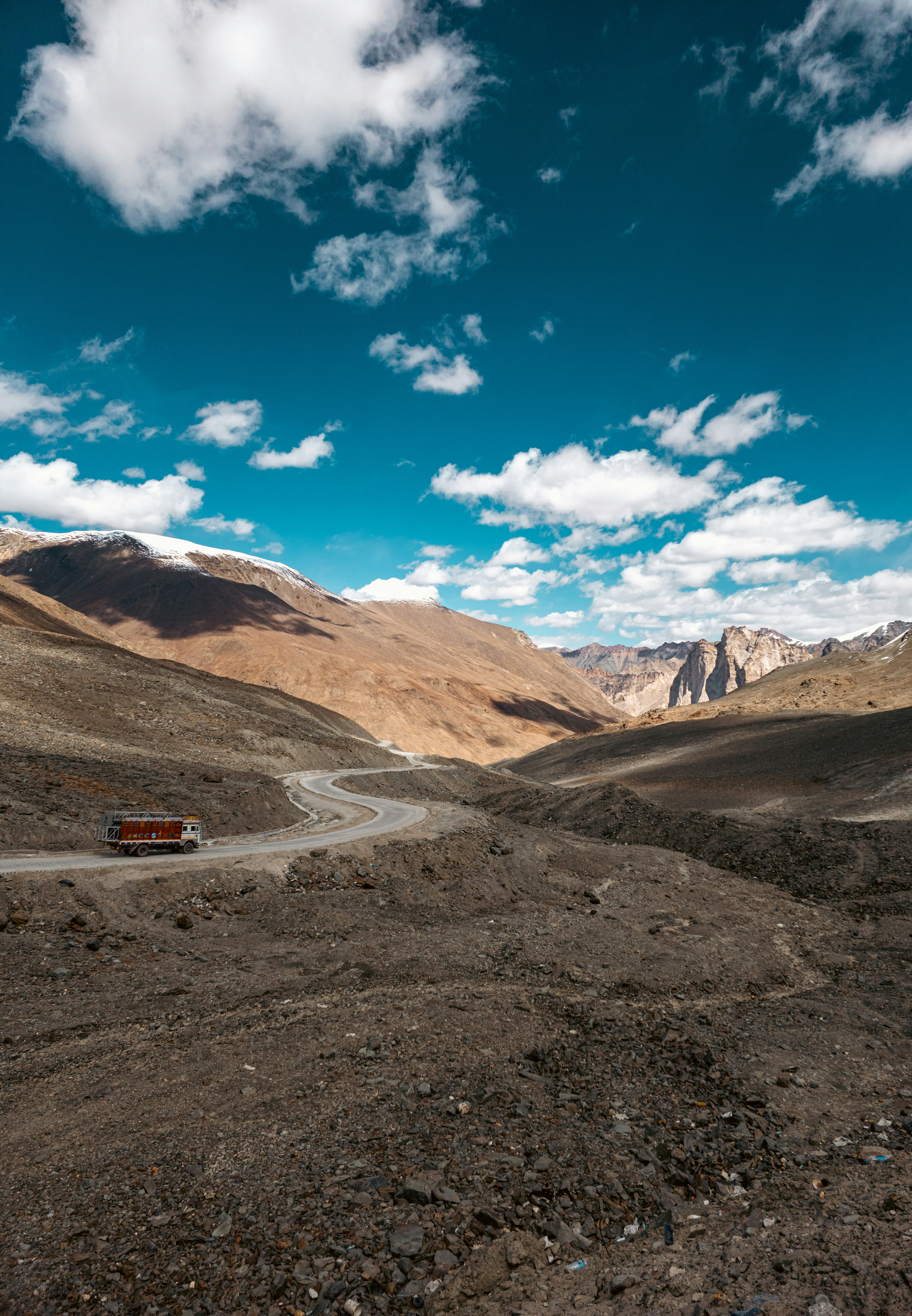 Winding mountain road with a vehicle under a blue sky.