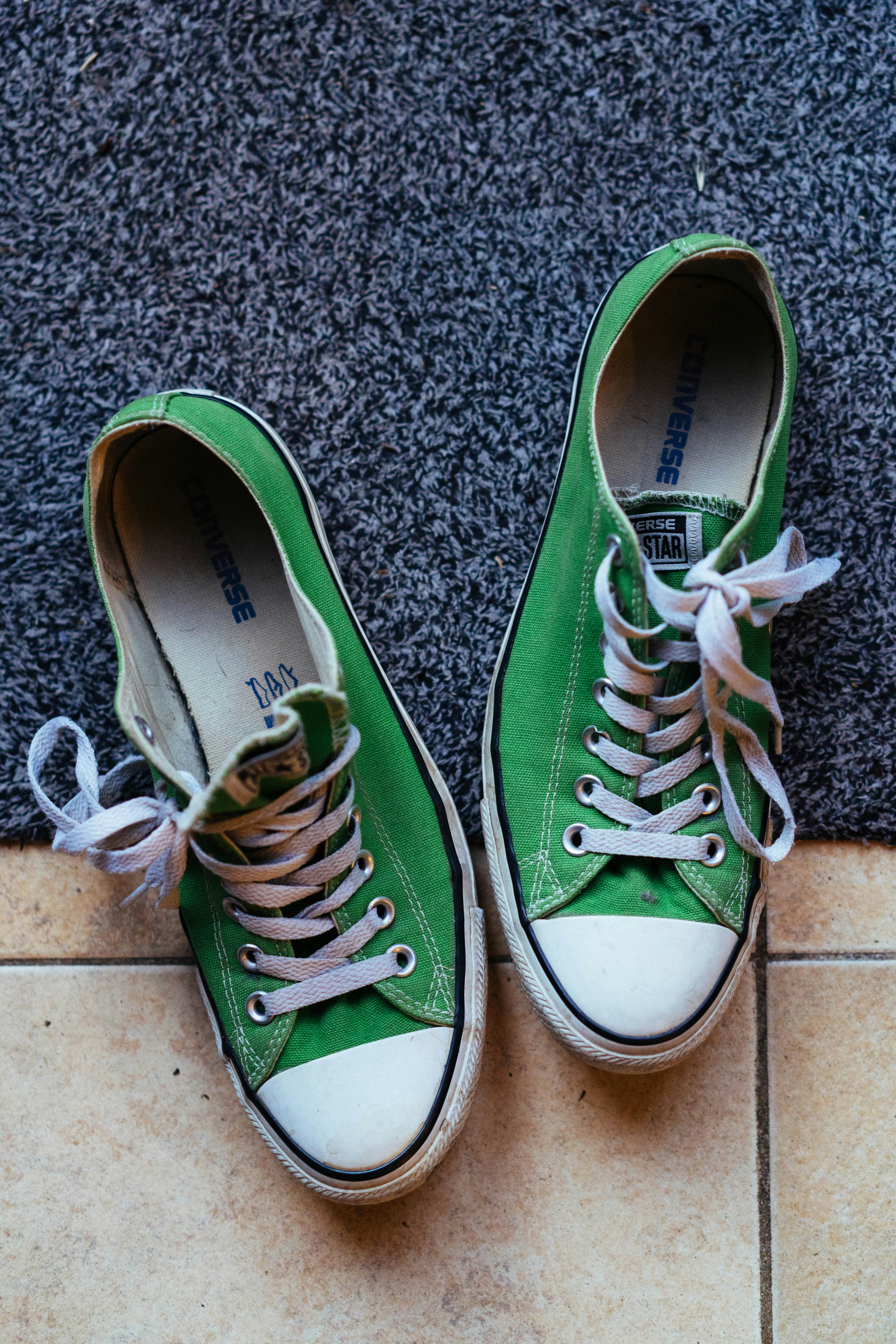 Green canvas shoes with white laces on a gray rug.
