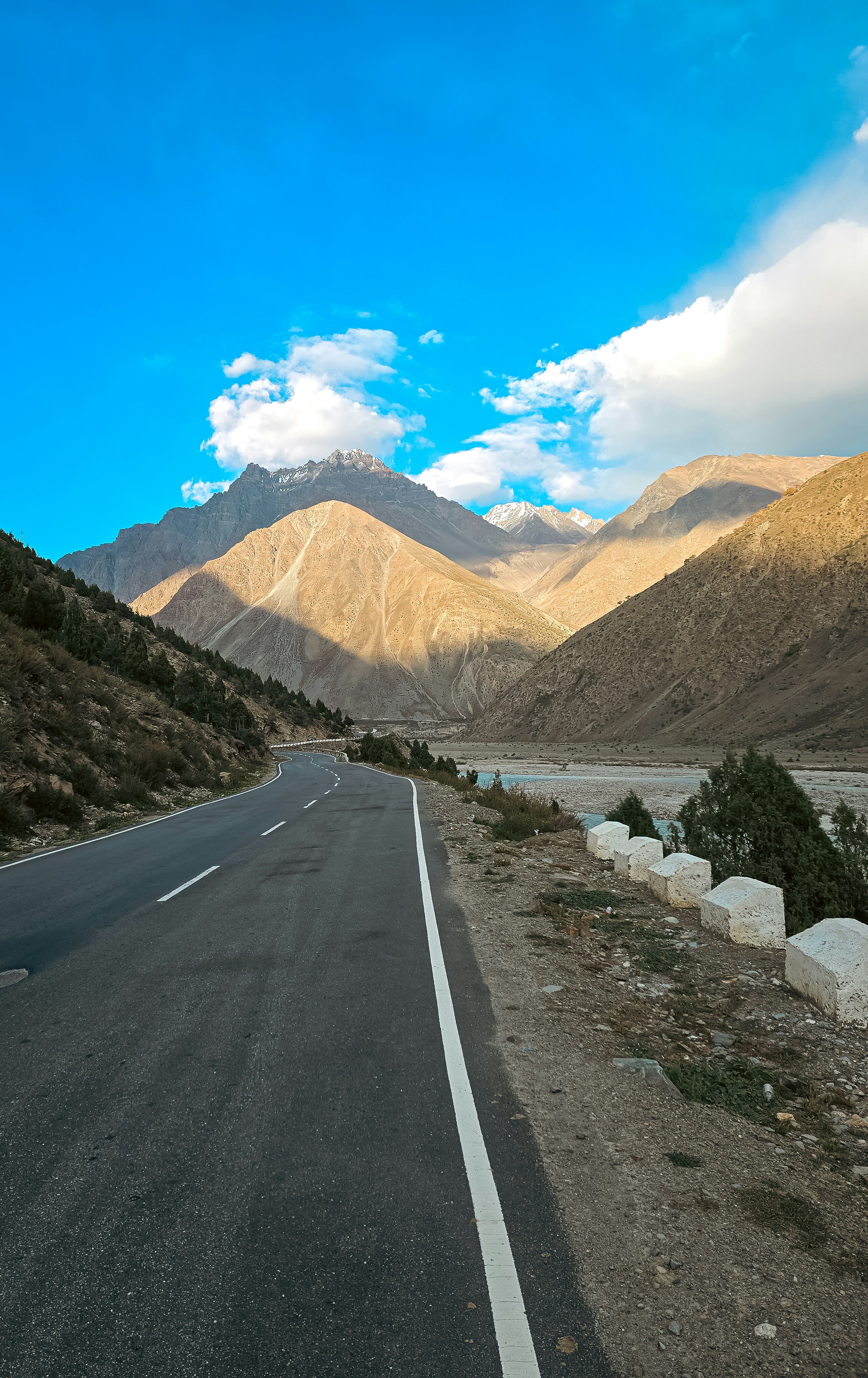 Scenic mountain road and river valley under blue sky.
