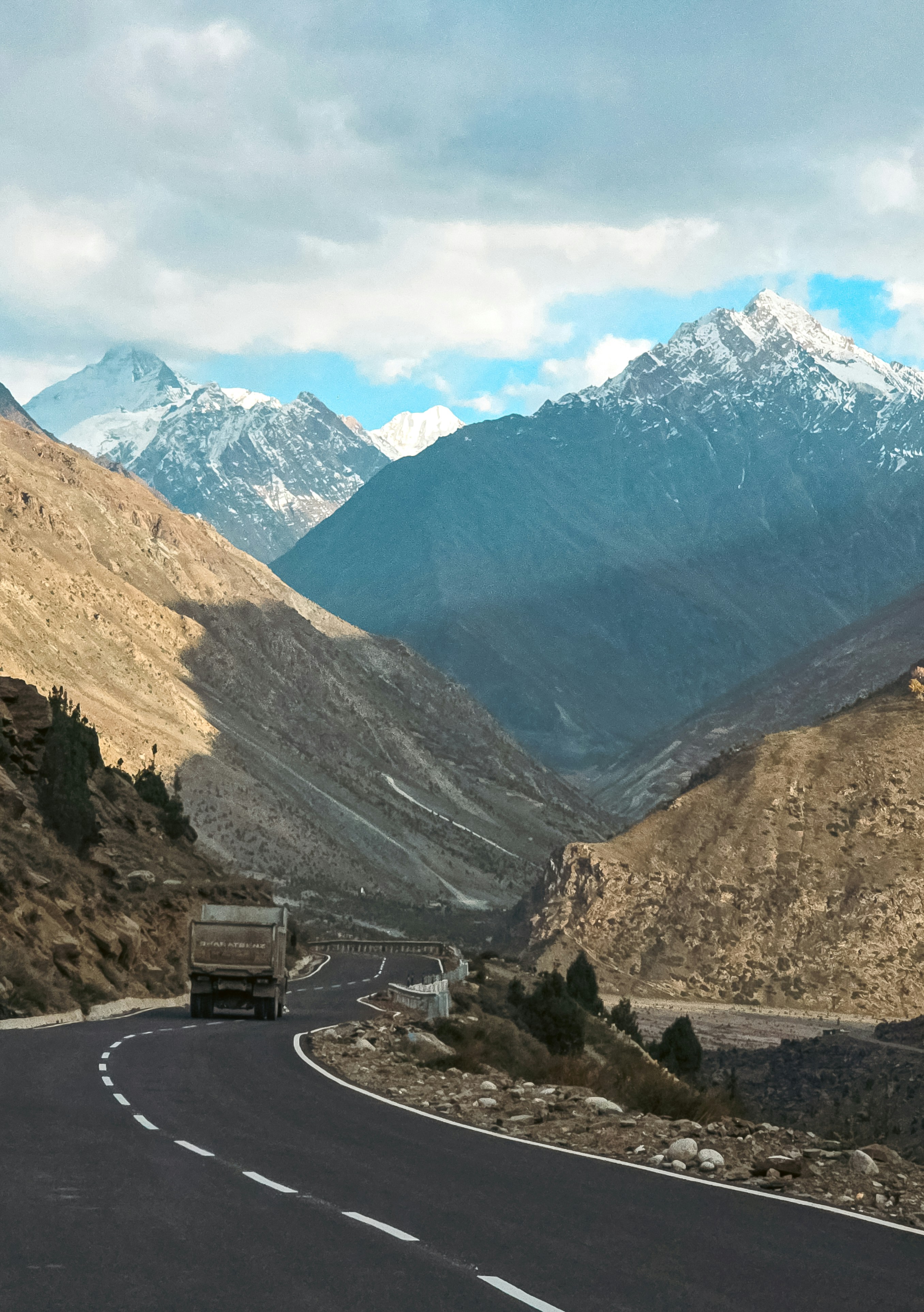 Truck on a winding mountain road with snow-capped peaks.