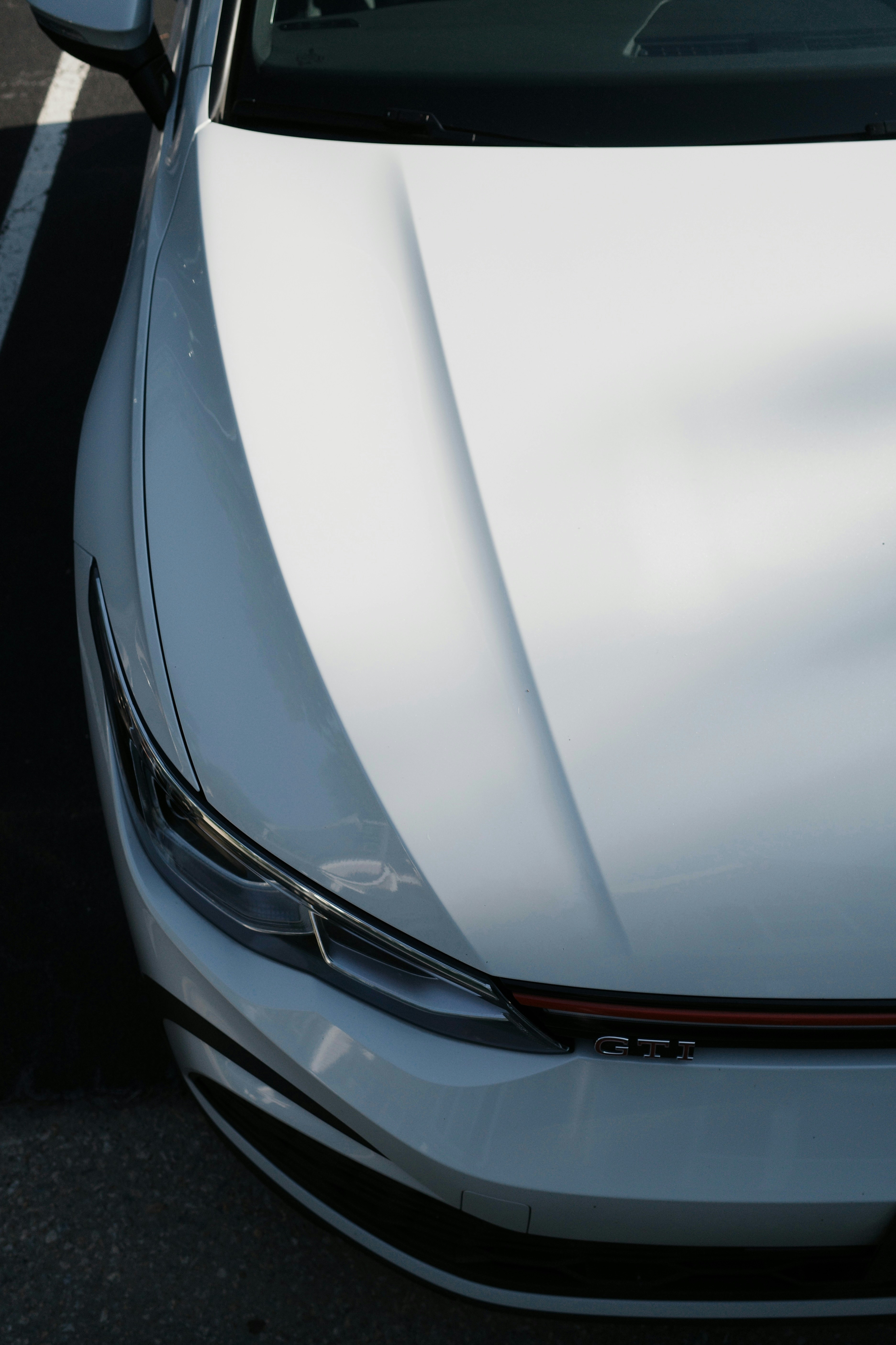 Weiße Front und Motorhaube des Wagens mit GTI-Emblem und Schatten.