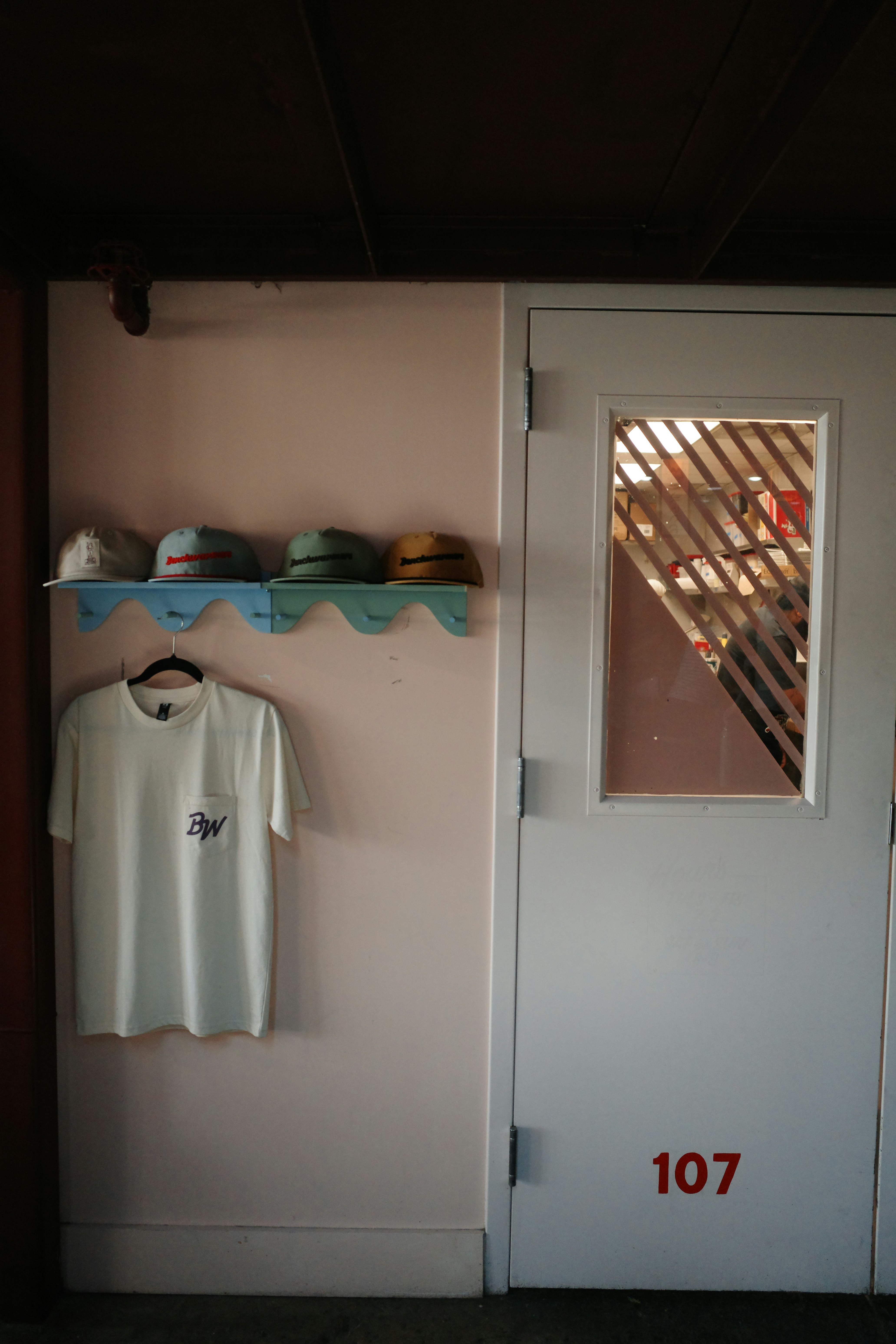 Rosa Wand mit Hüten, weißem T-Shirt und Tür 107.