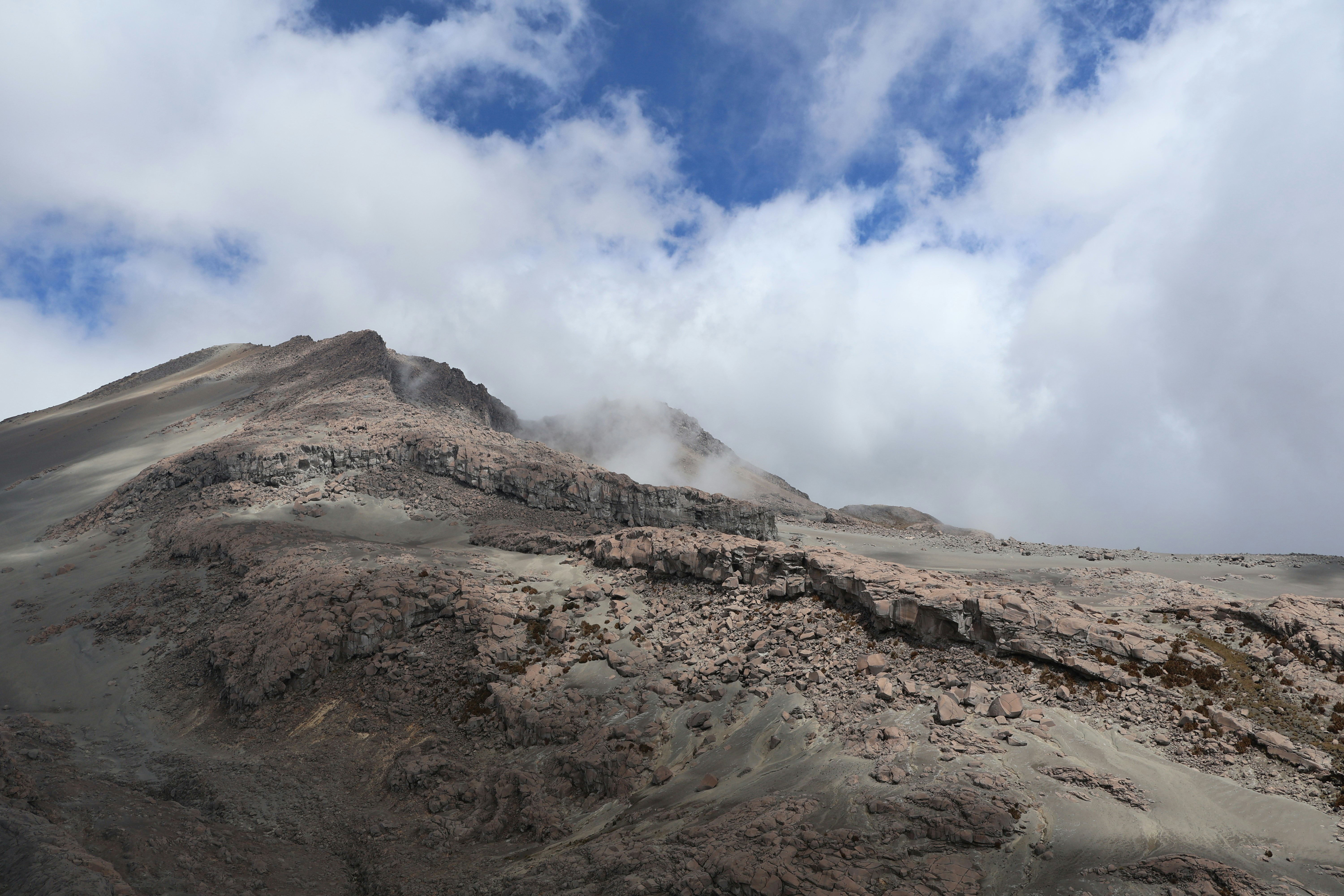 Volcanic mountain summit shrouded in clouds under blue sky.