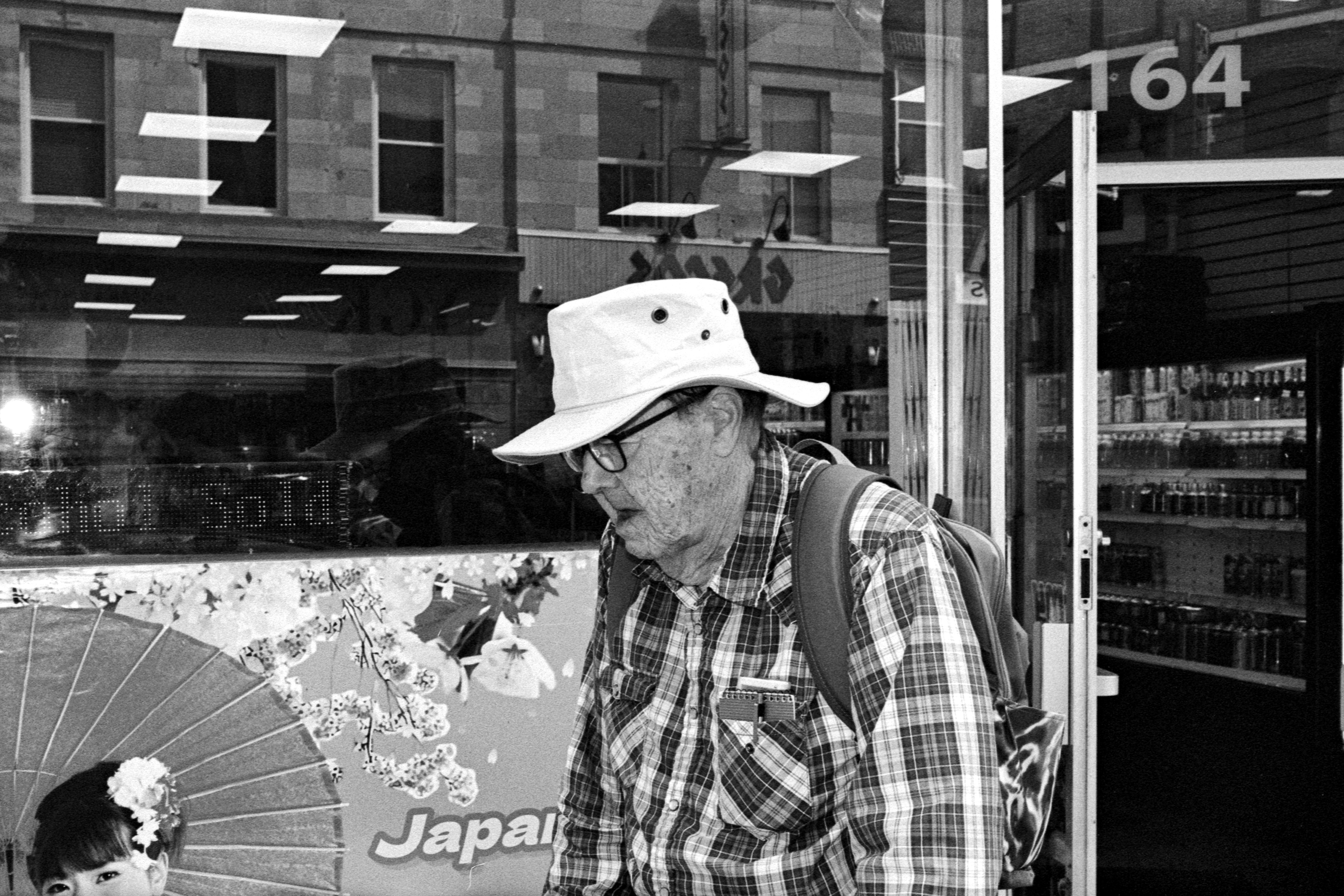 Man in hat and plaid shirt walks past city storefront