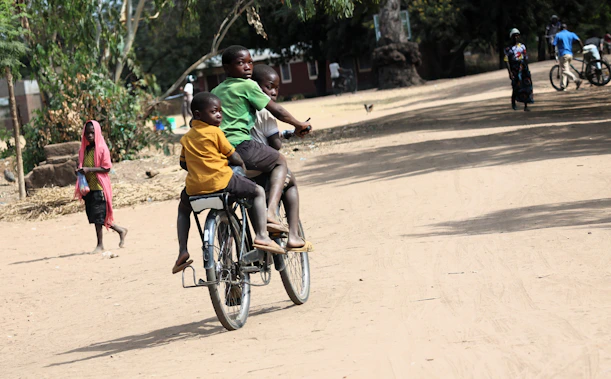 Two children ride a bicycle on a dirt road