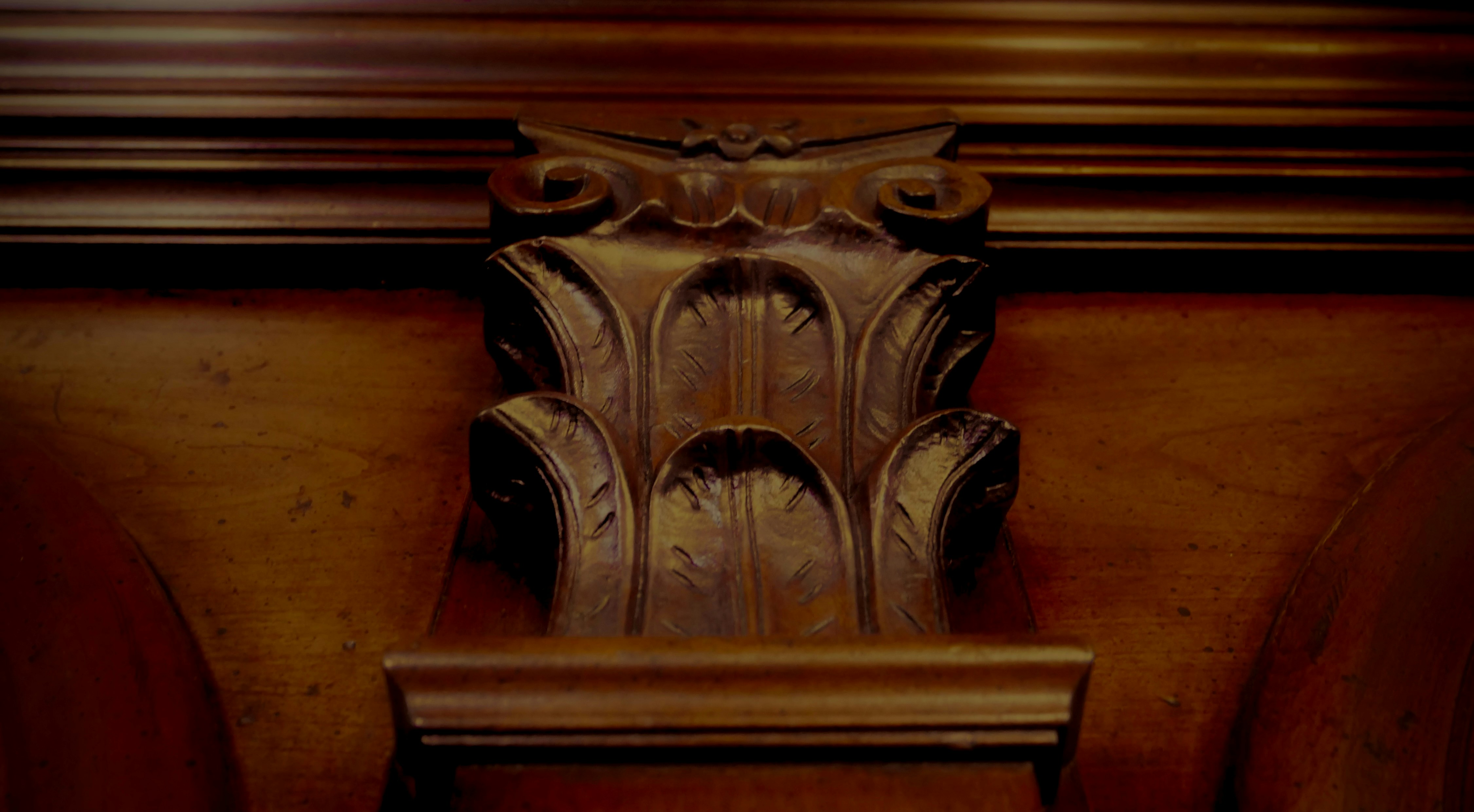 Carved wooden corinthian capital detail on a dark wood panel.