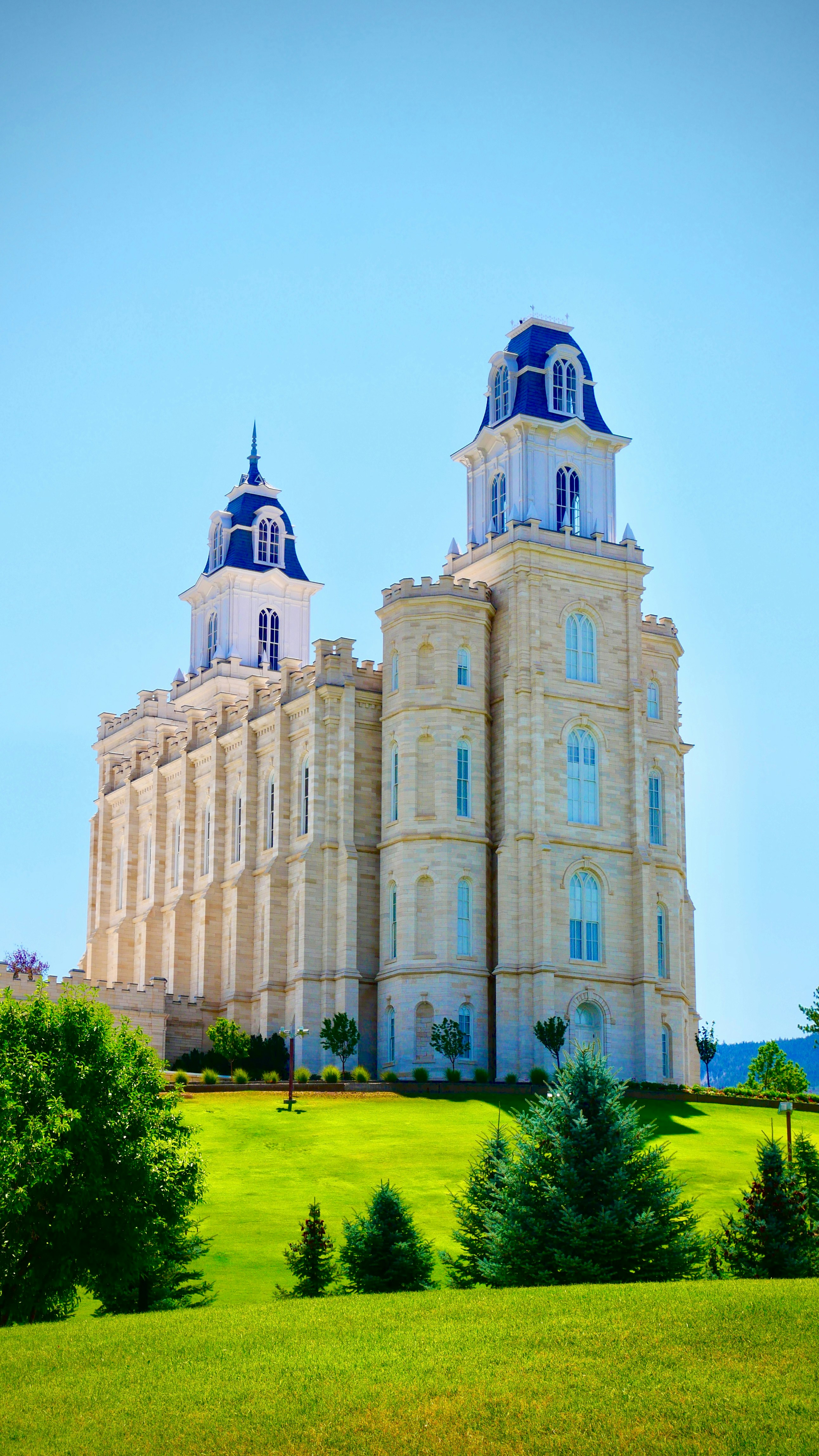 Ornate temple with blue spires on a vibrant green hillside.
