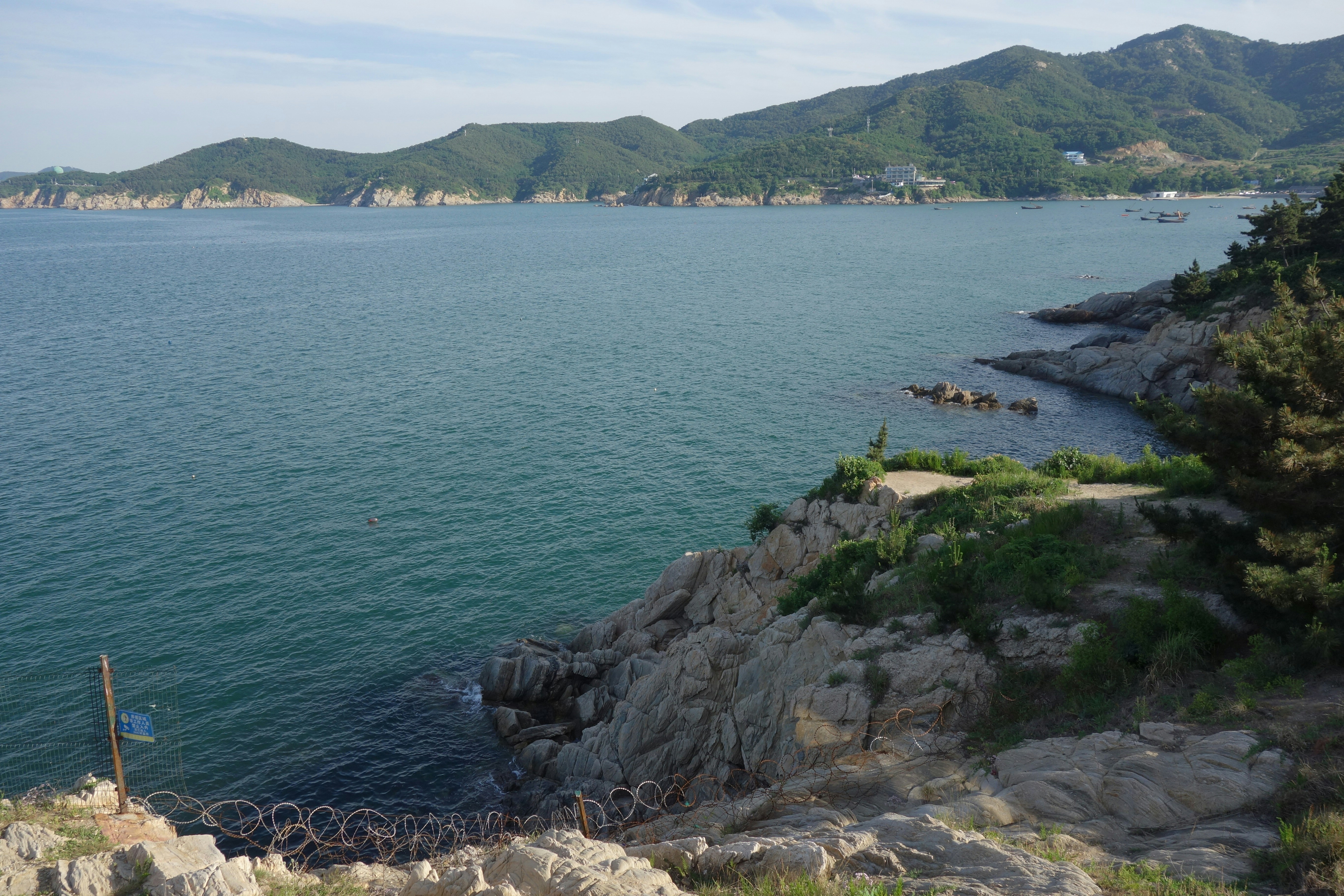 Rocky coastline overlooking a calm bay with distant green mountains.