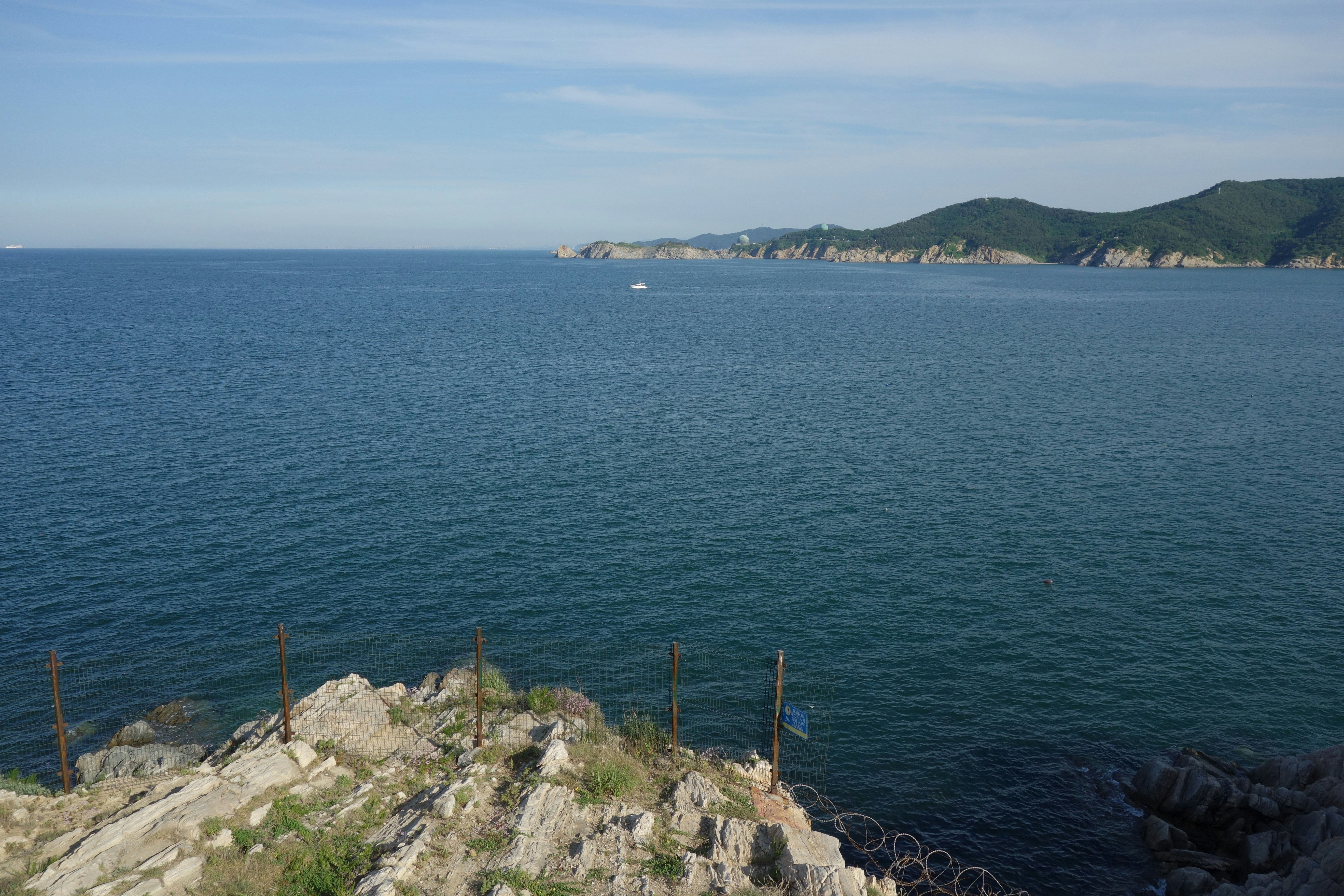 Vast blue ocean with rocky foreground and distant green coastline