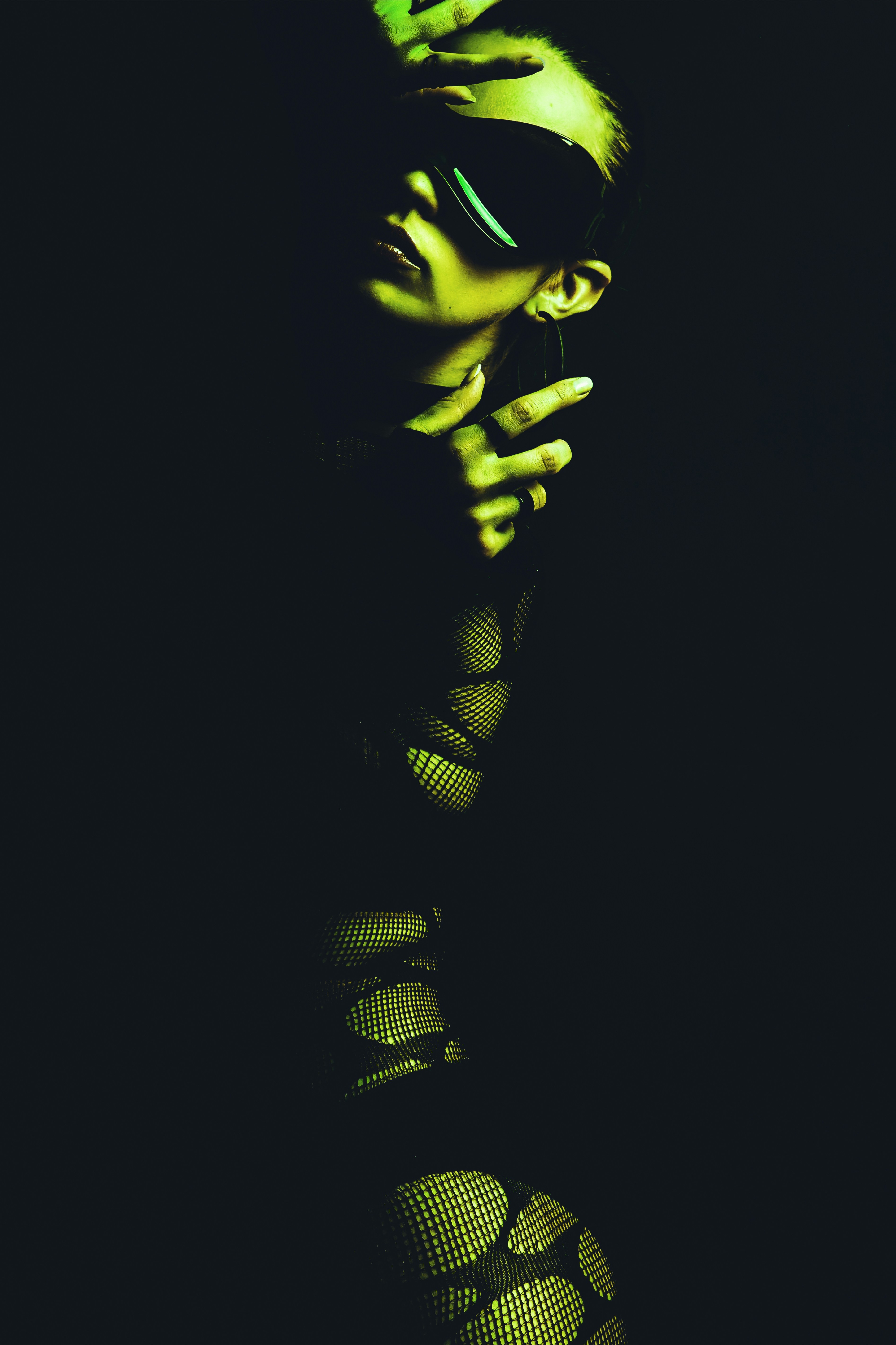 Woman in fishnet outfit and blindfold under green light.