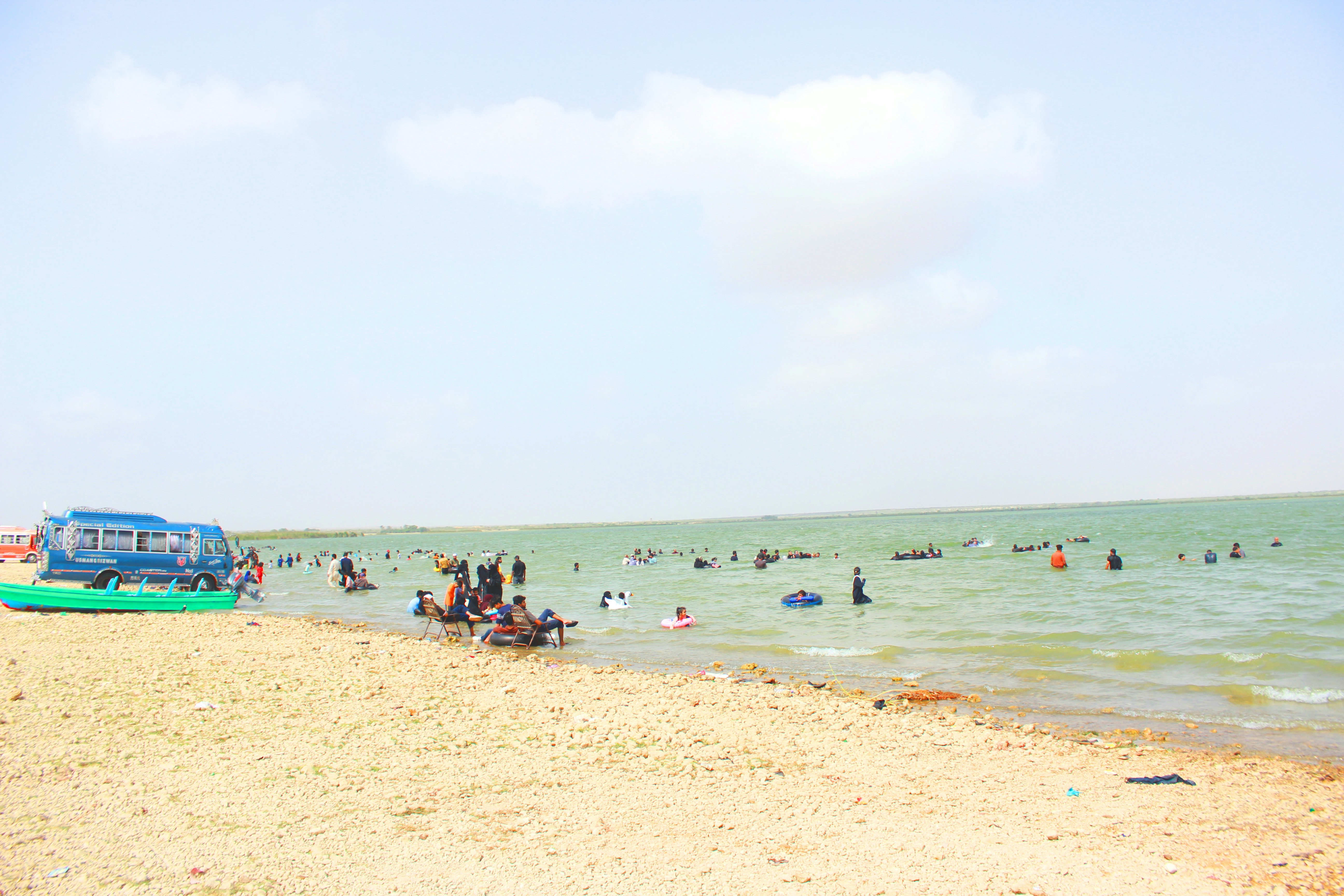 Una playa de arena con gente nadando y un autobús aparcado.