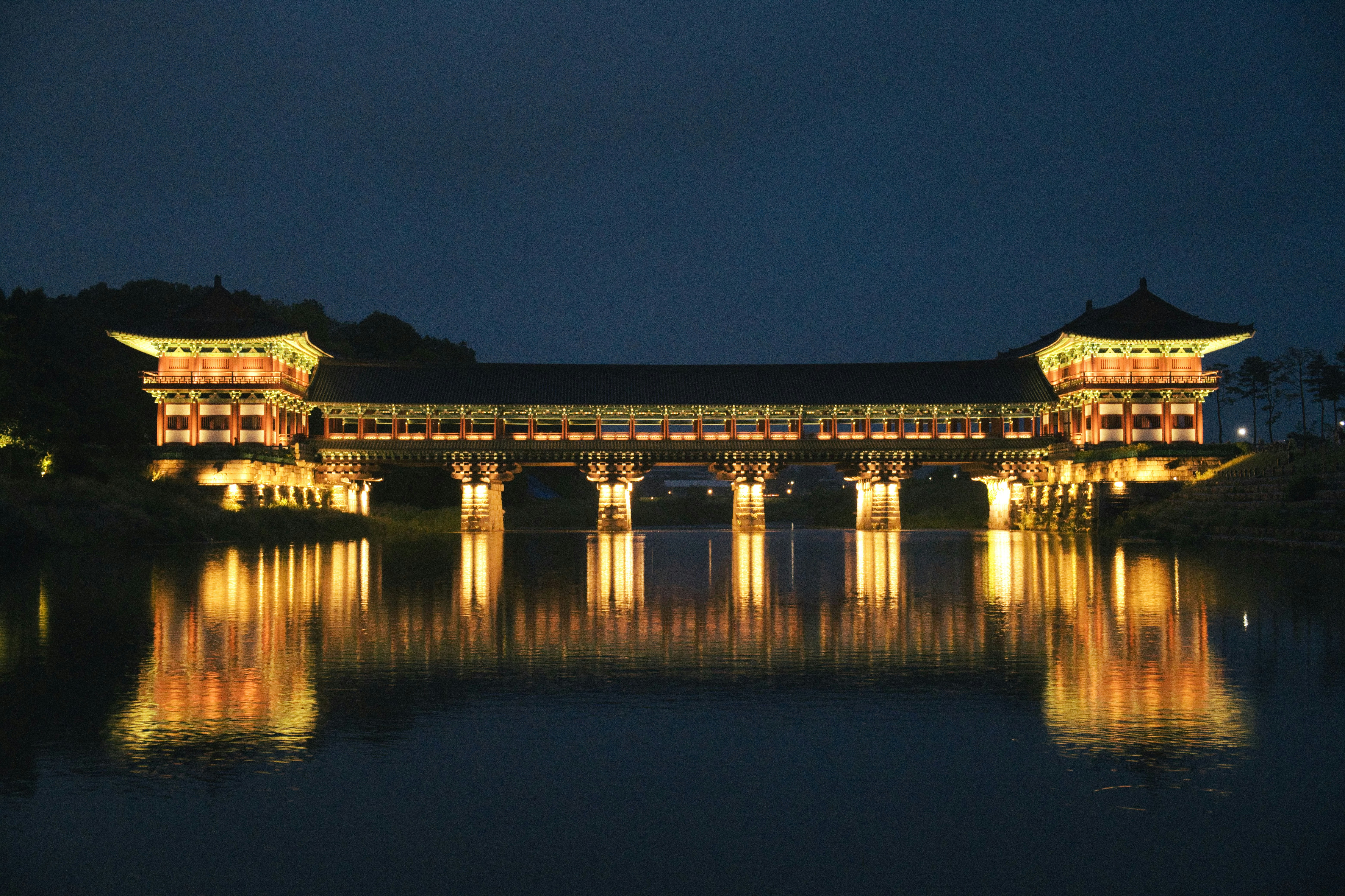 Puente asiático tradicional iluminado por la noche reflejado en aguas tranquilas.