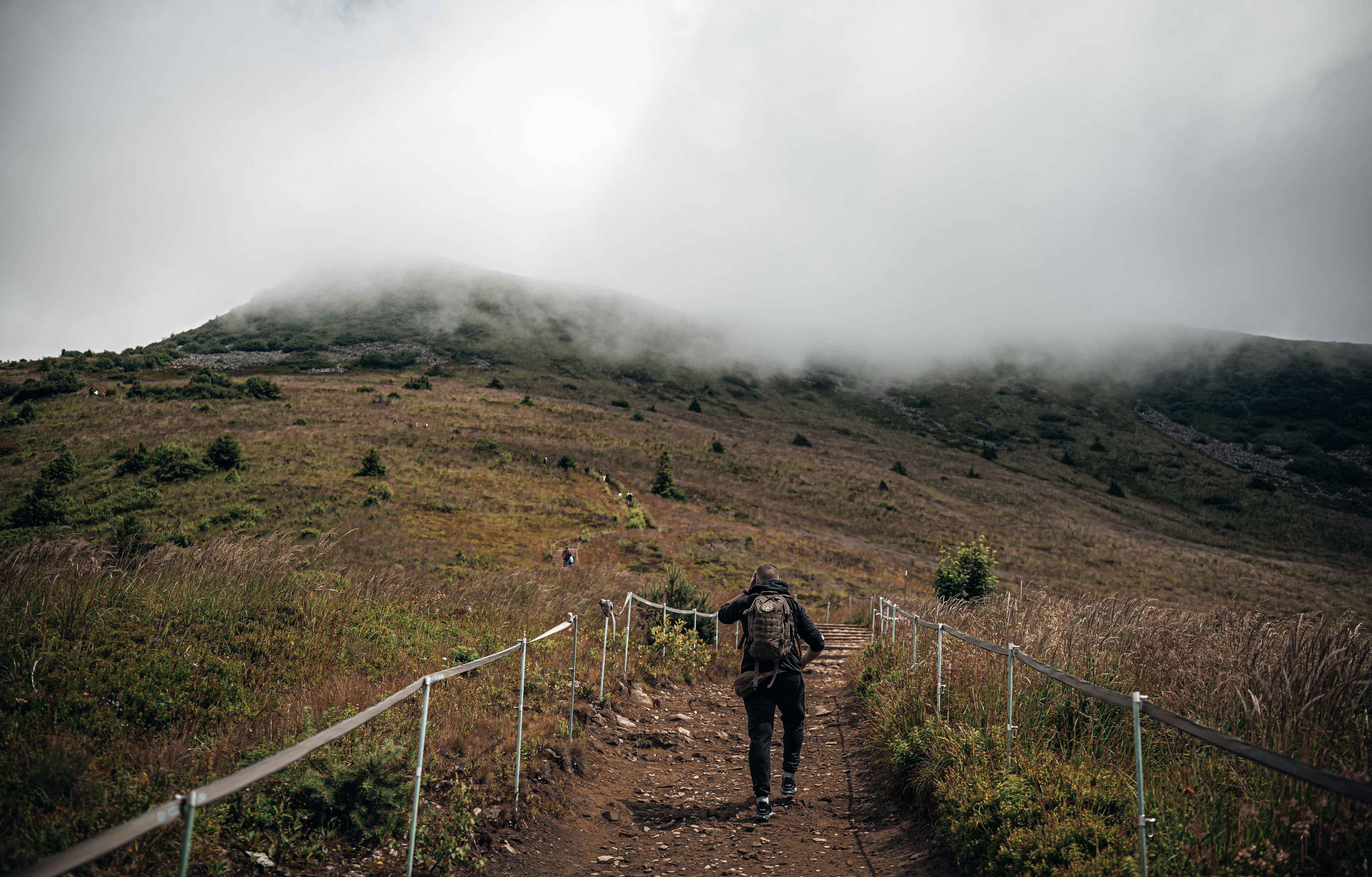 A person hikes a foggy mountain path.