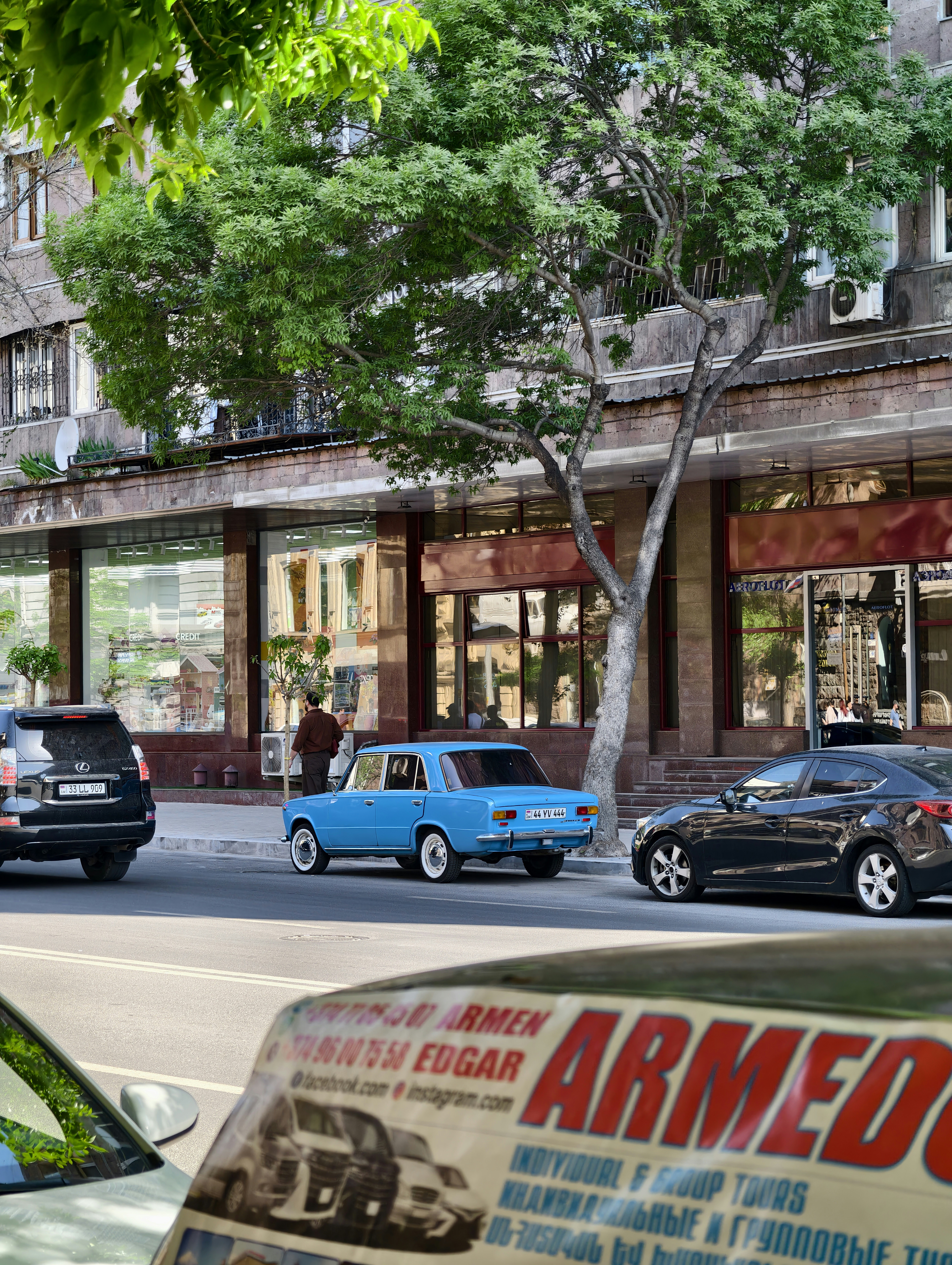A blue vintage car drives down a city street.