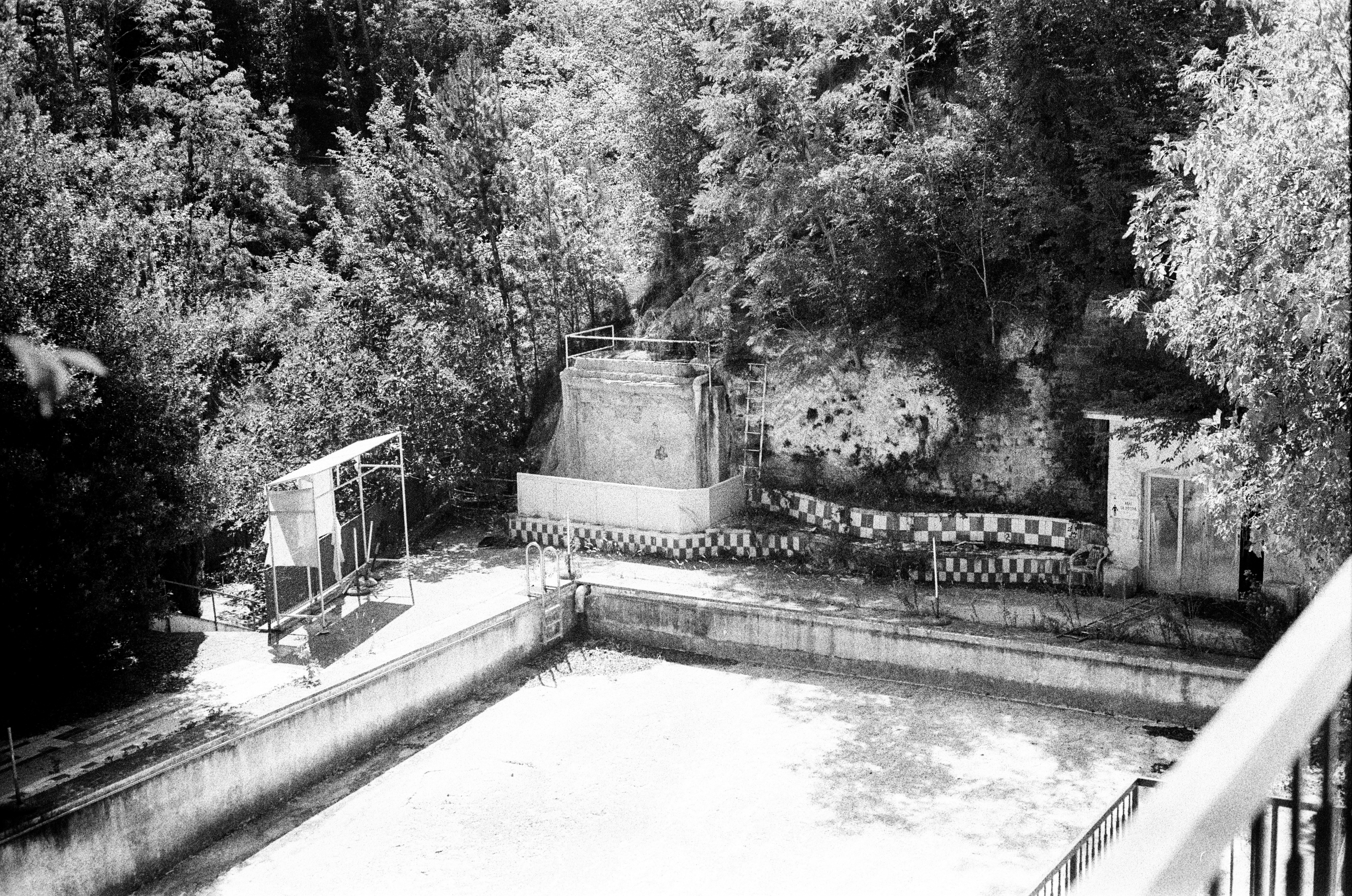 A drained old swimming pool with checkered tiles on a wooded hillside