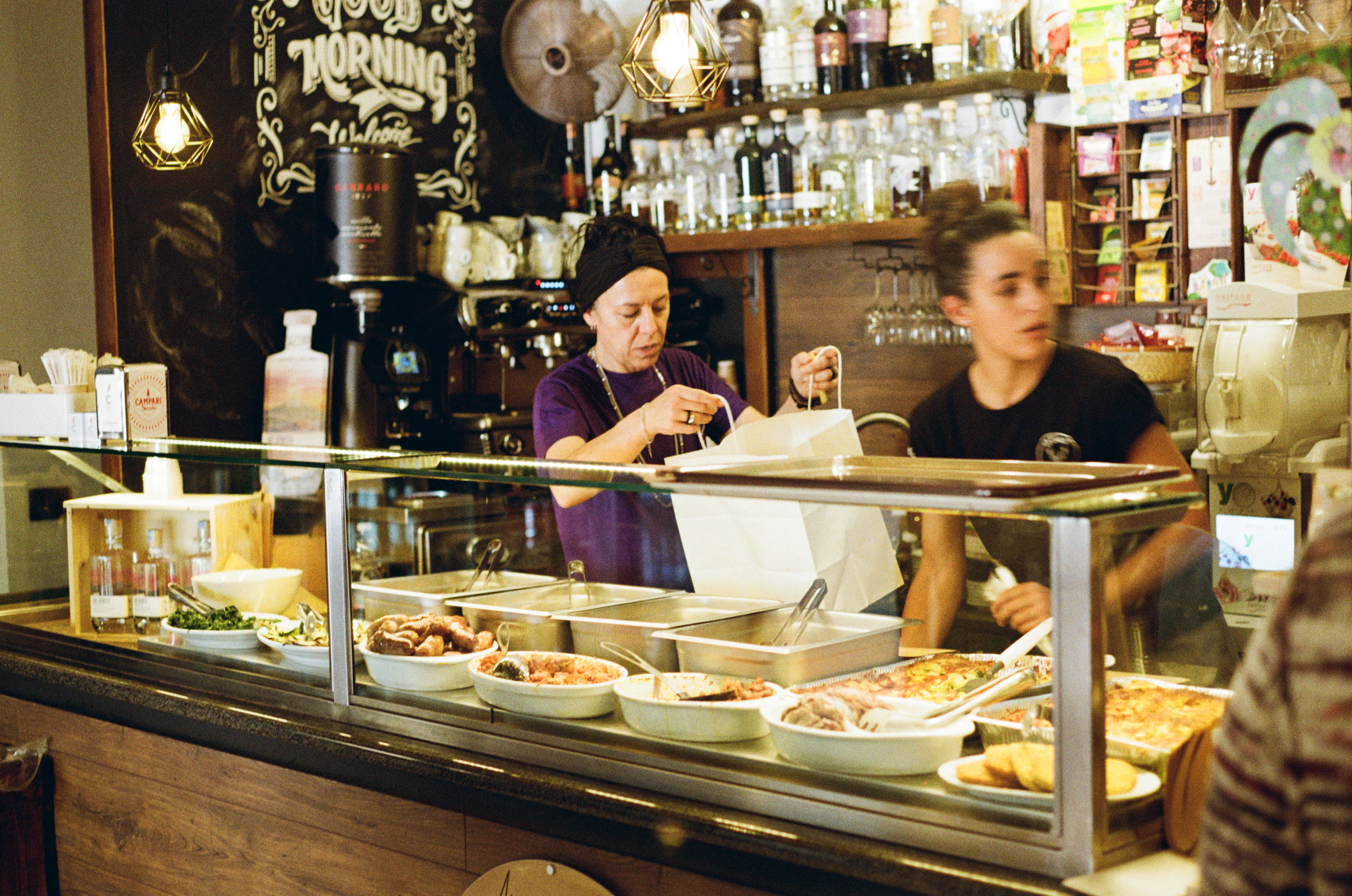 Two people working behind a busy hot food deli counter