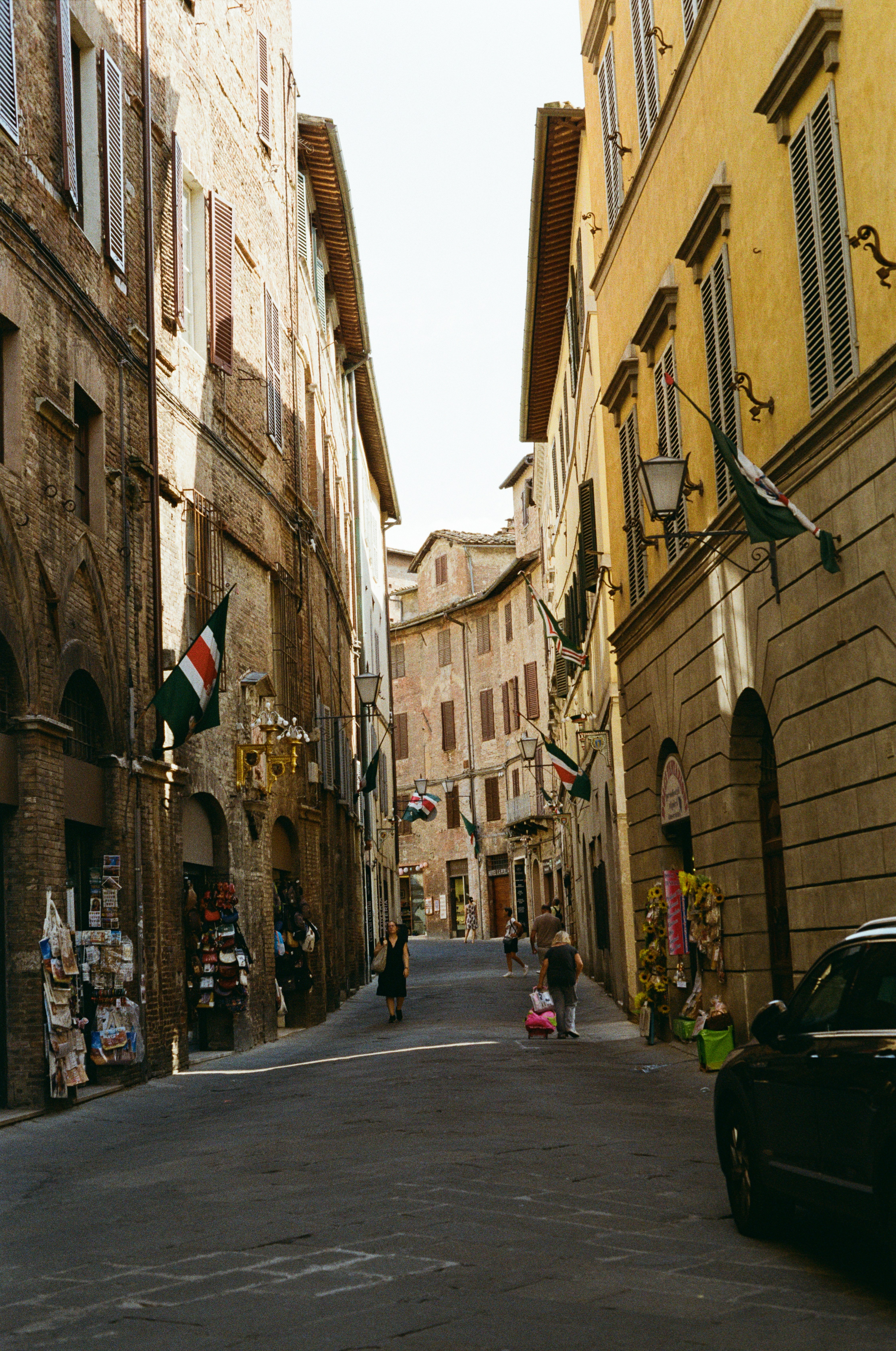 Stretta via di Siena con edifici storici e bandiere contrada