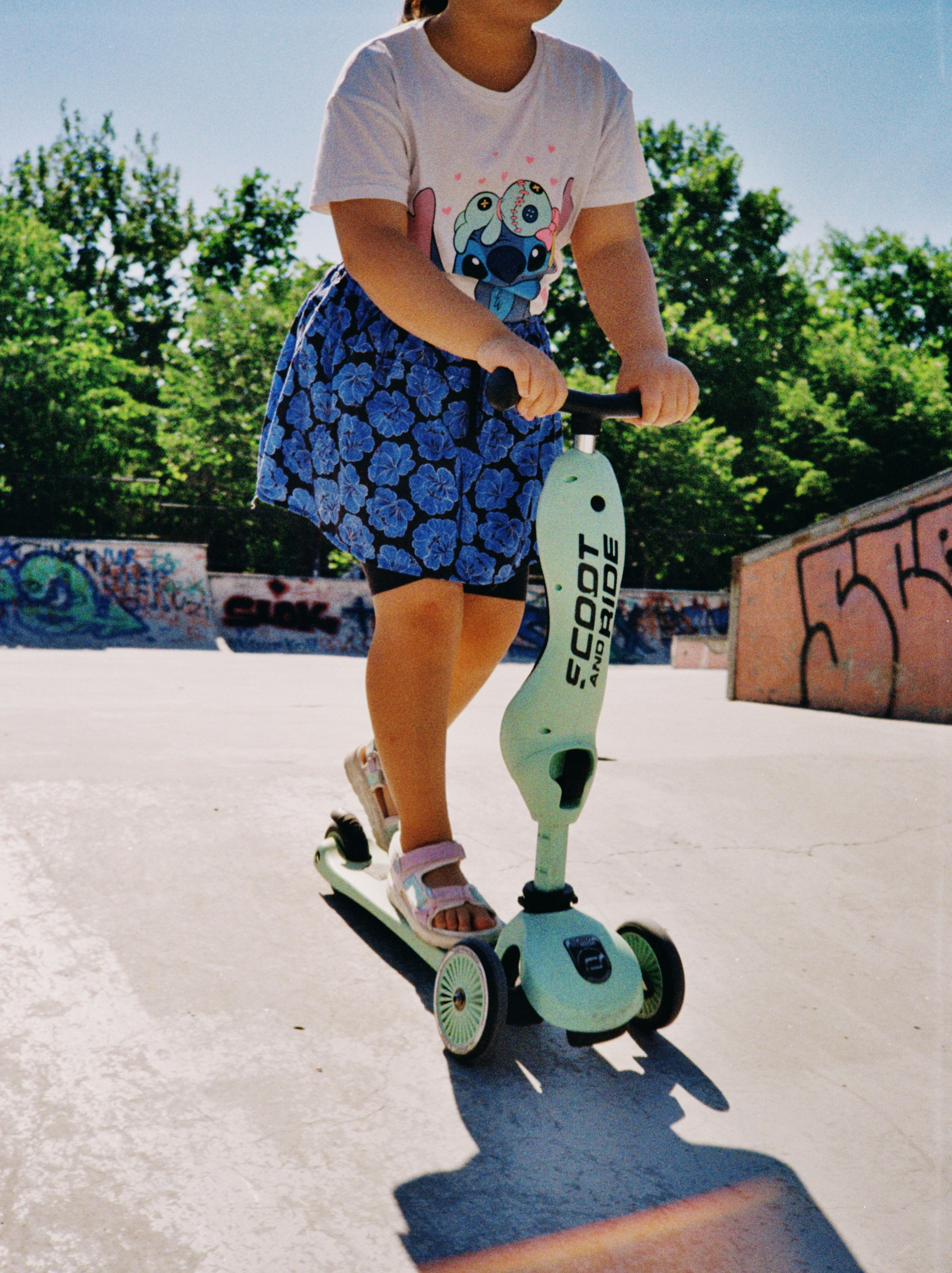 Young girl riding a scooter in a sunny skate park.