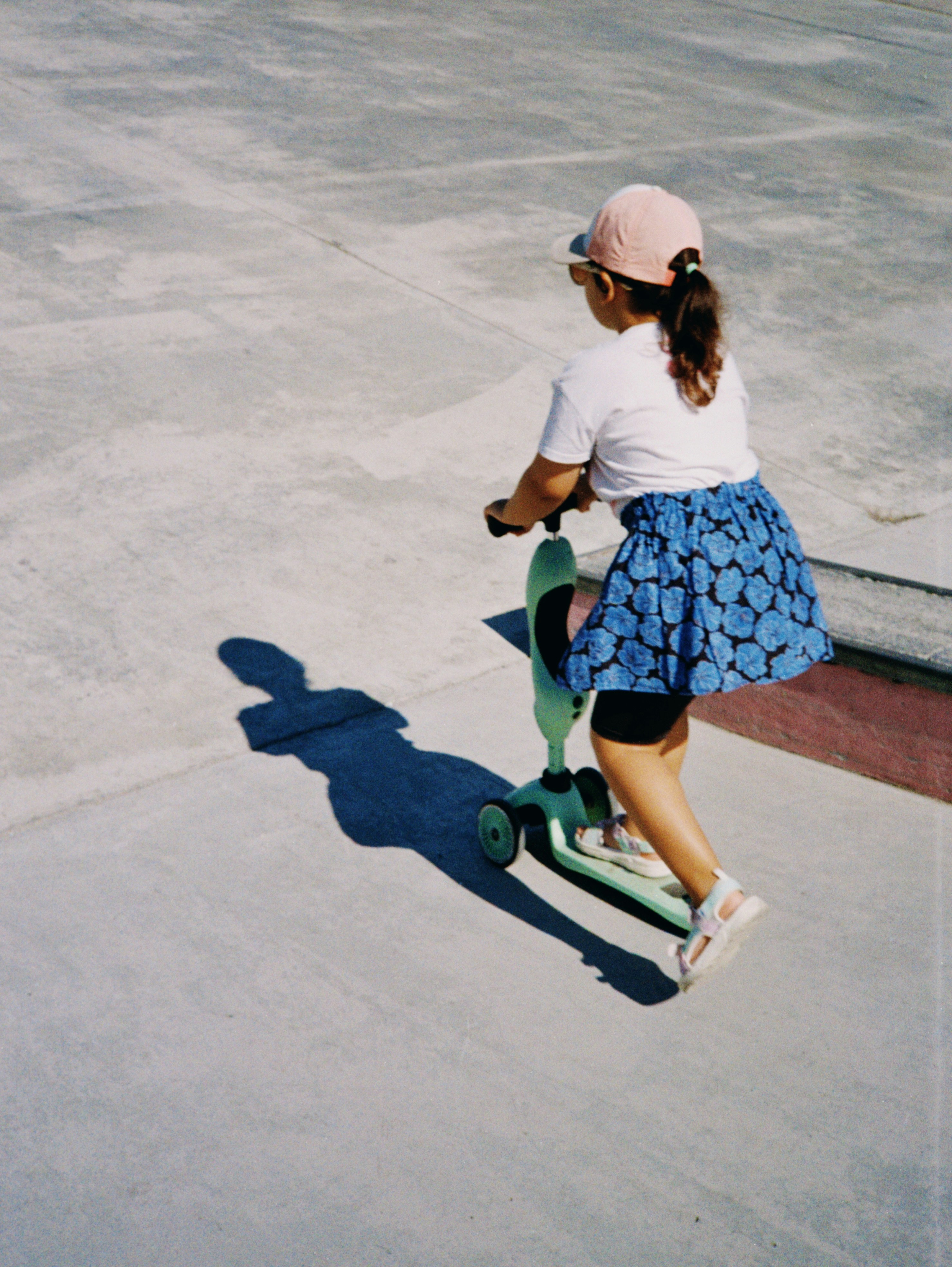 A young girl rides a green scooter on concrete.