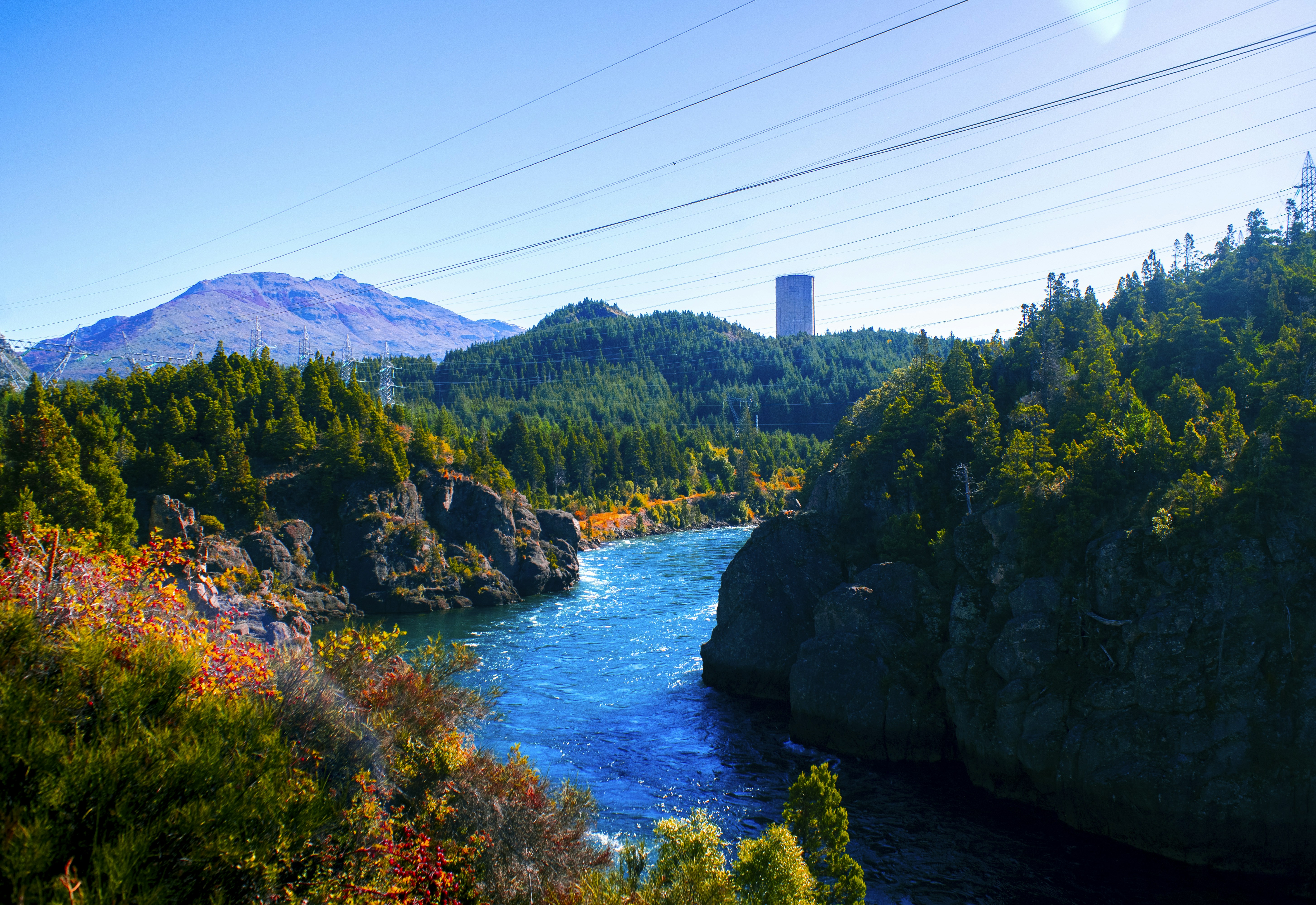 Vibrant blue river flows through a forested canyon with mountains.