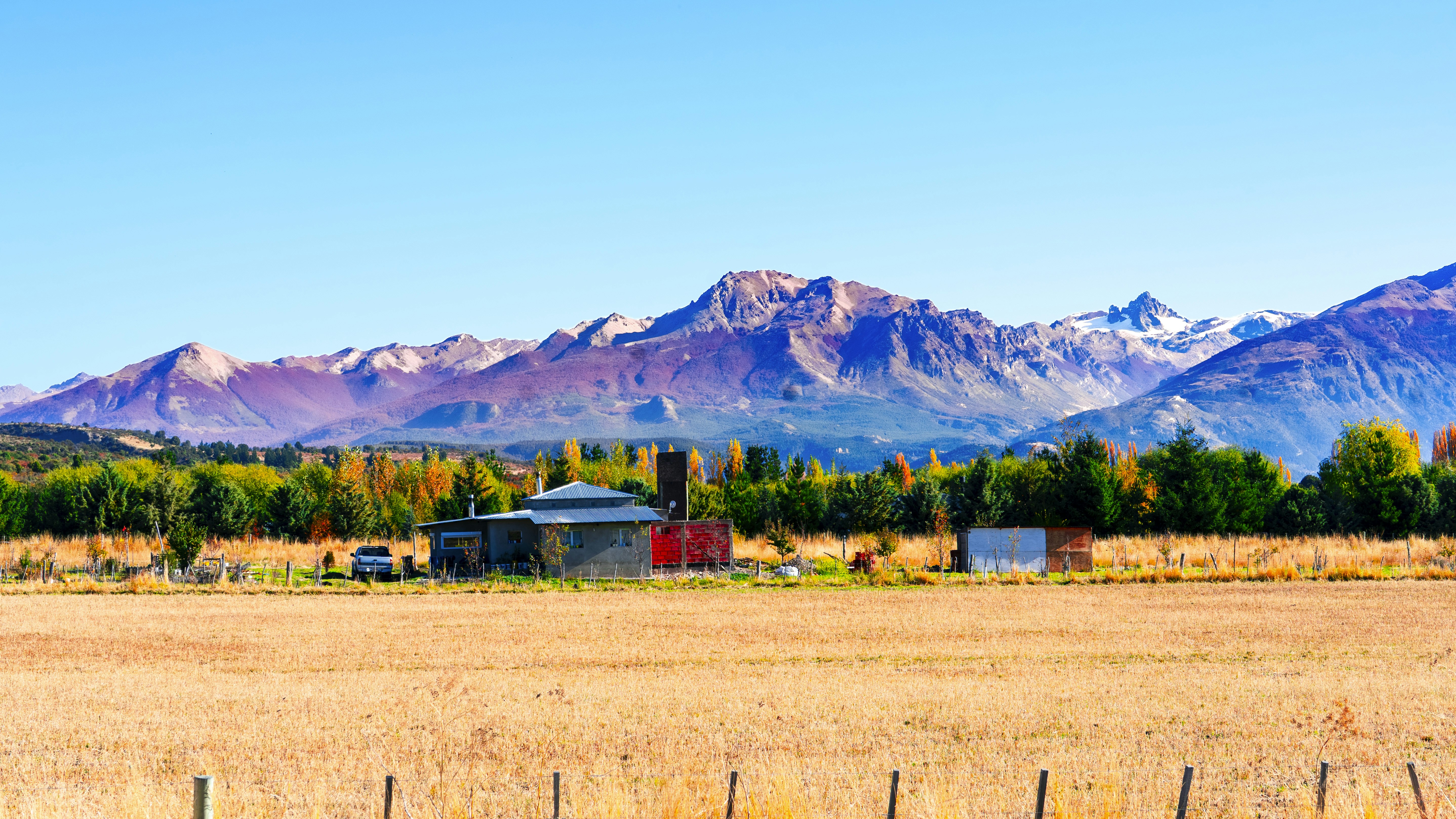 Golden field, farm buildings, colorful autumn trees, and mountains.