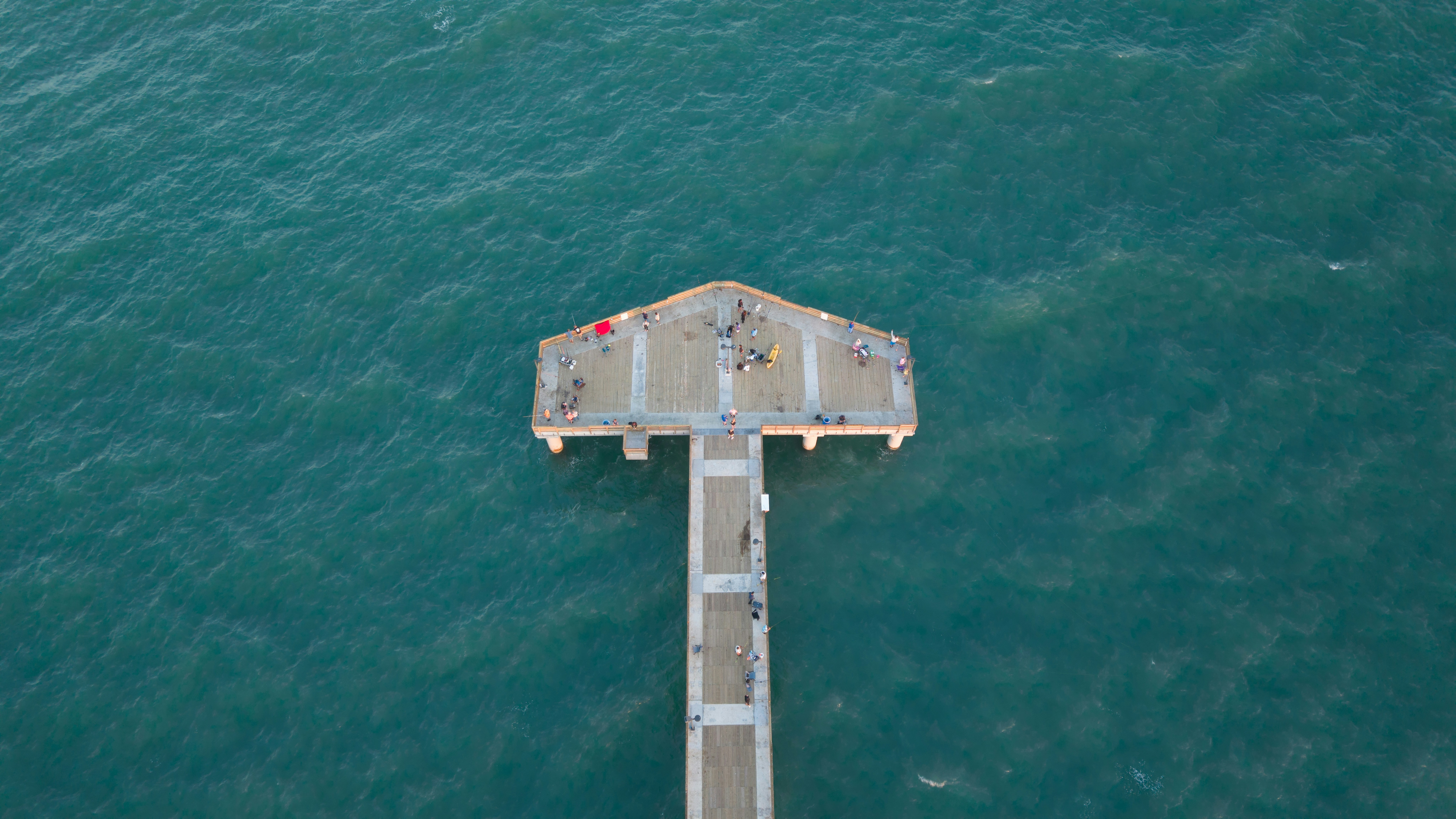 People on a concrete pier in the vast blue ocean.