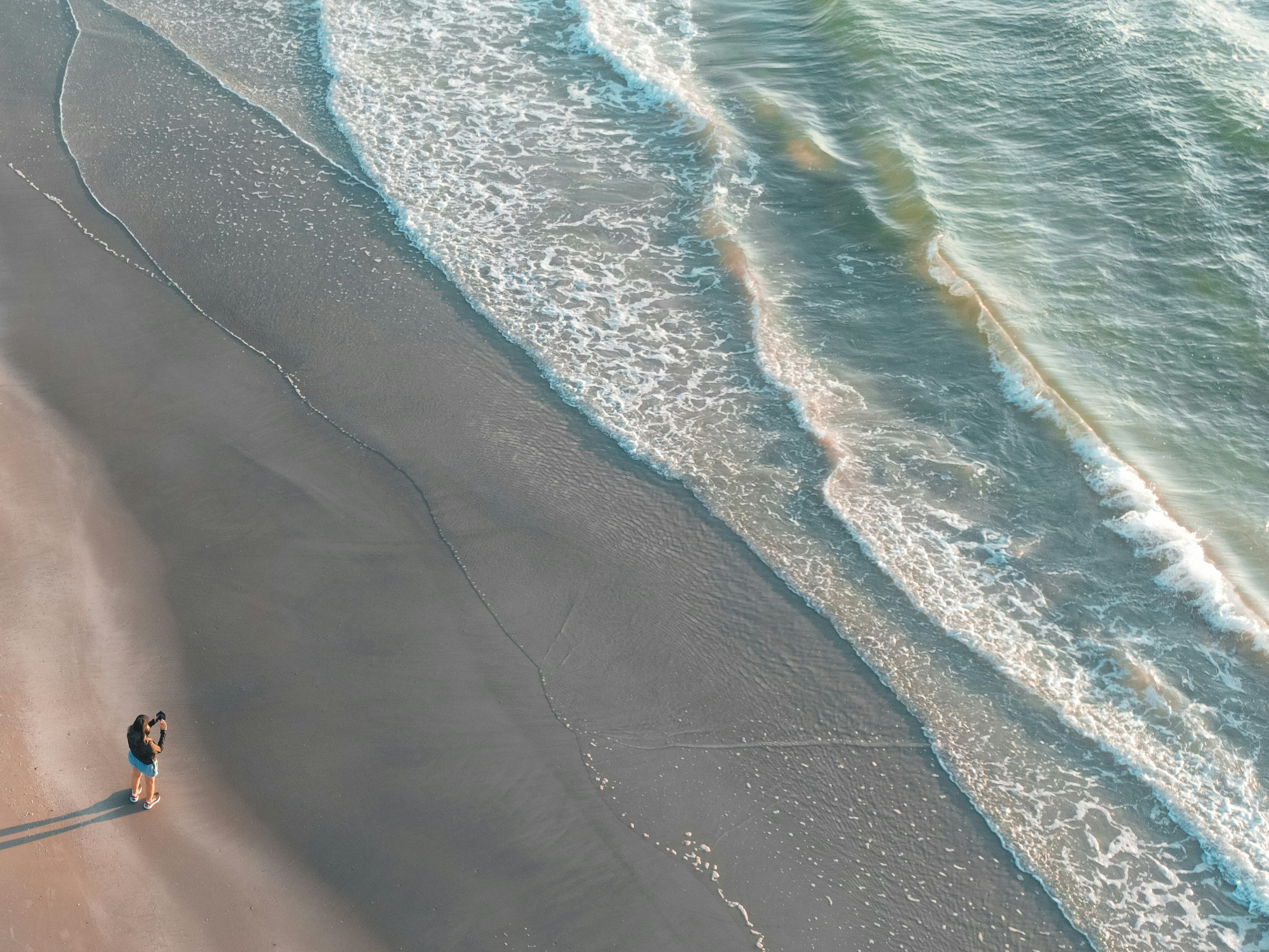 Person standing on a sandy beach with ocean waves.