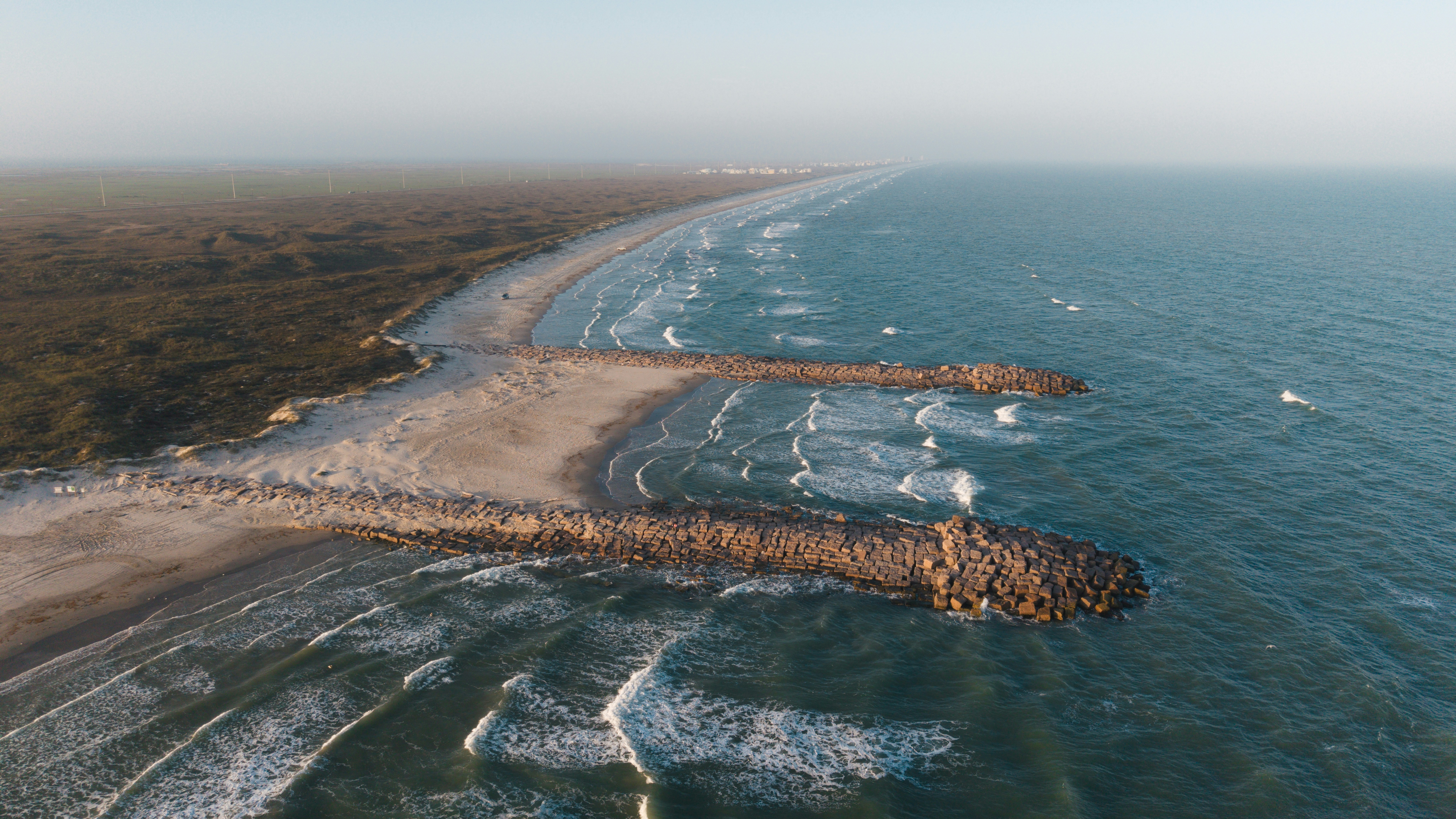 Ocean waves crashing on a sandy beach with two jetties.