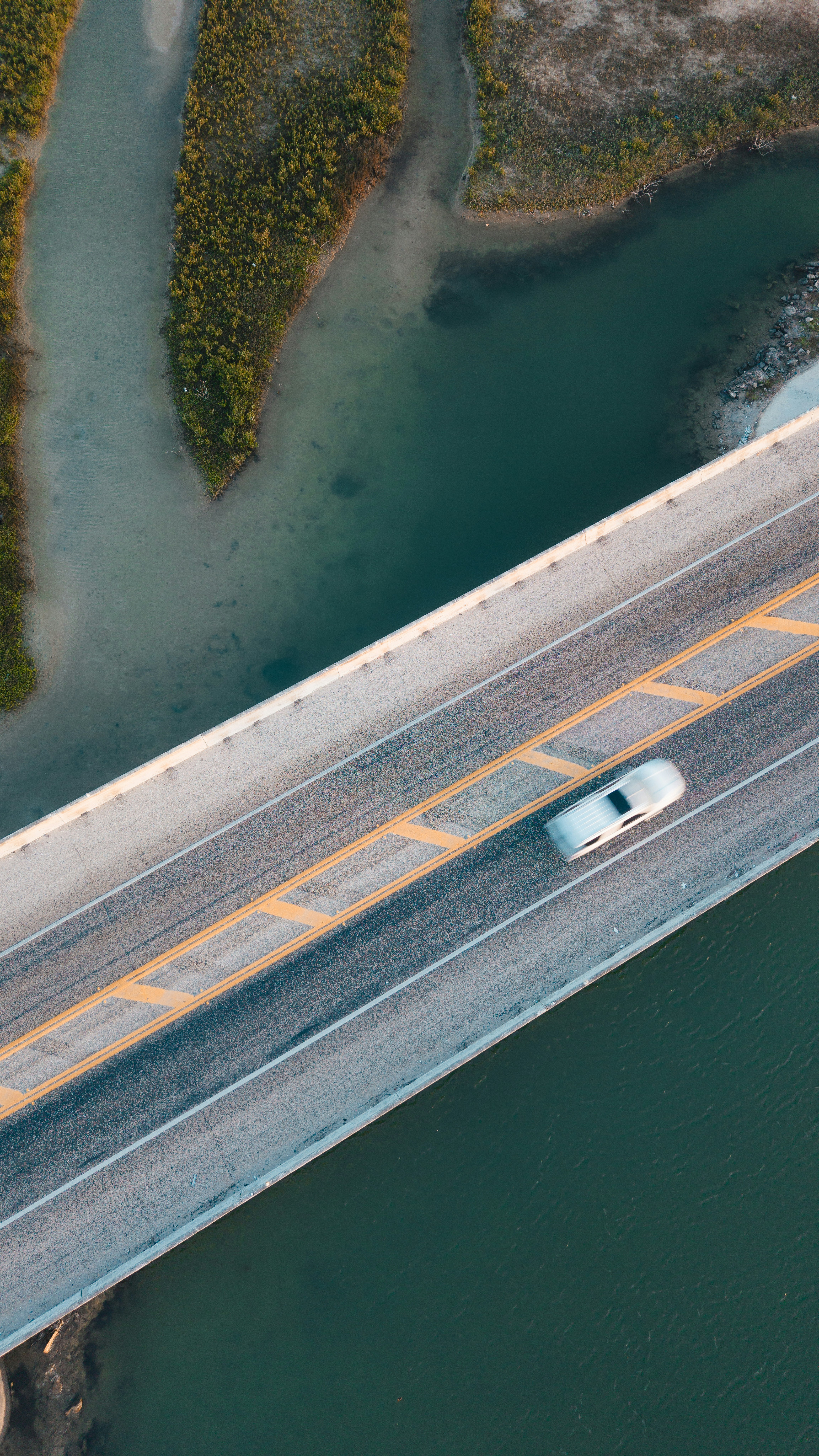 Car on a bridge spanning a river and green land.