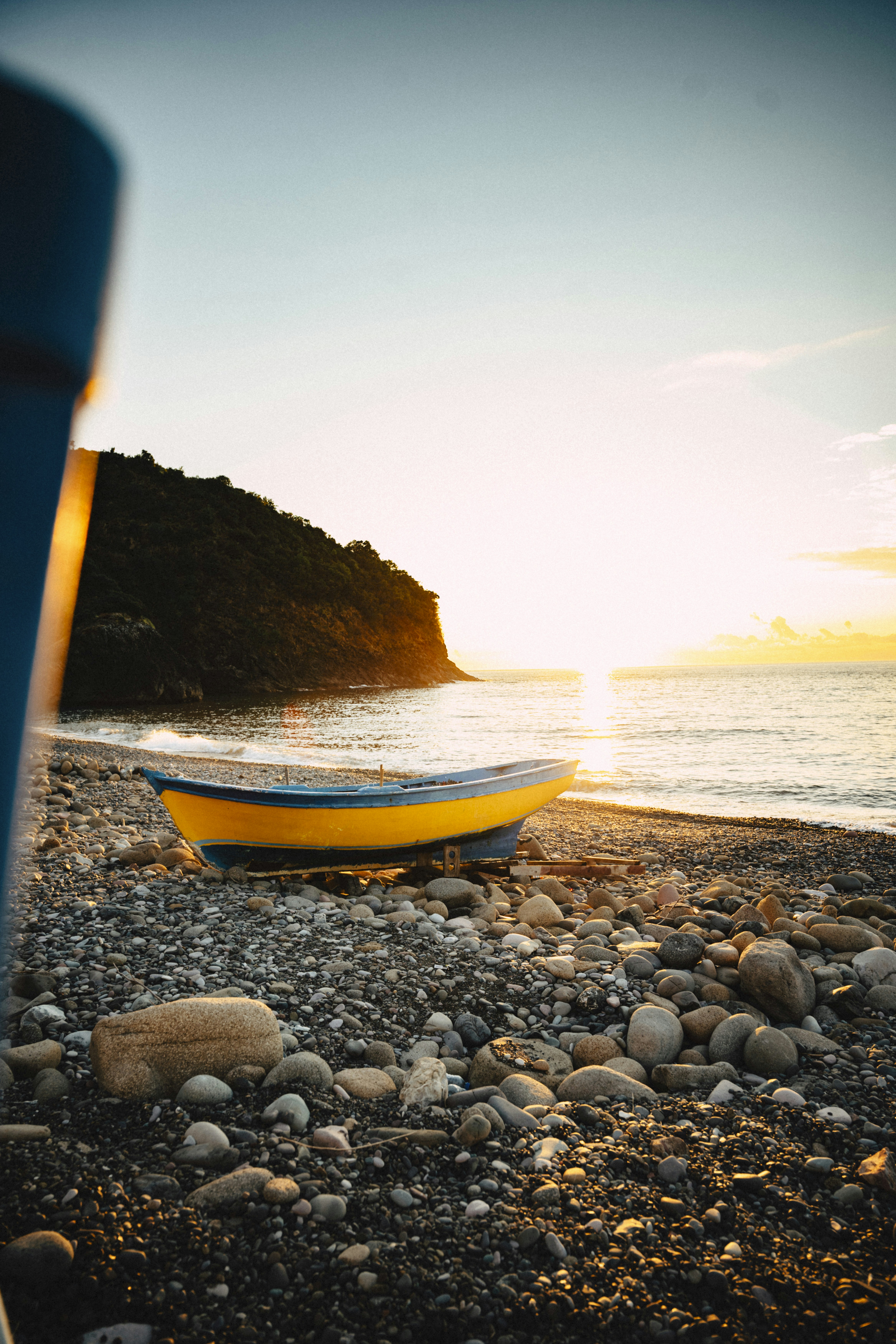 Barco amarelo na praia rochosa ao pôr do sol