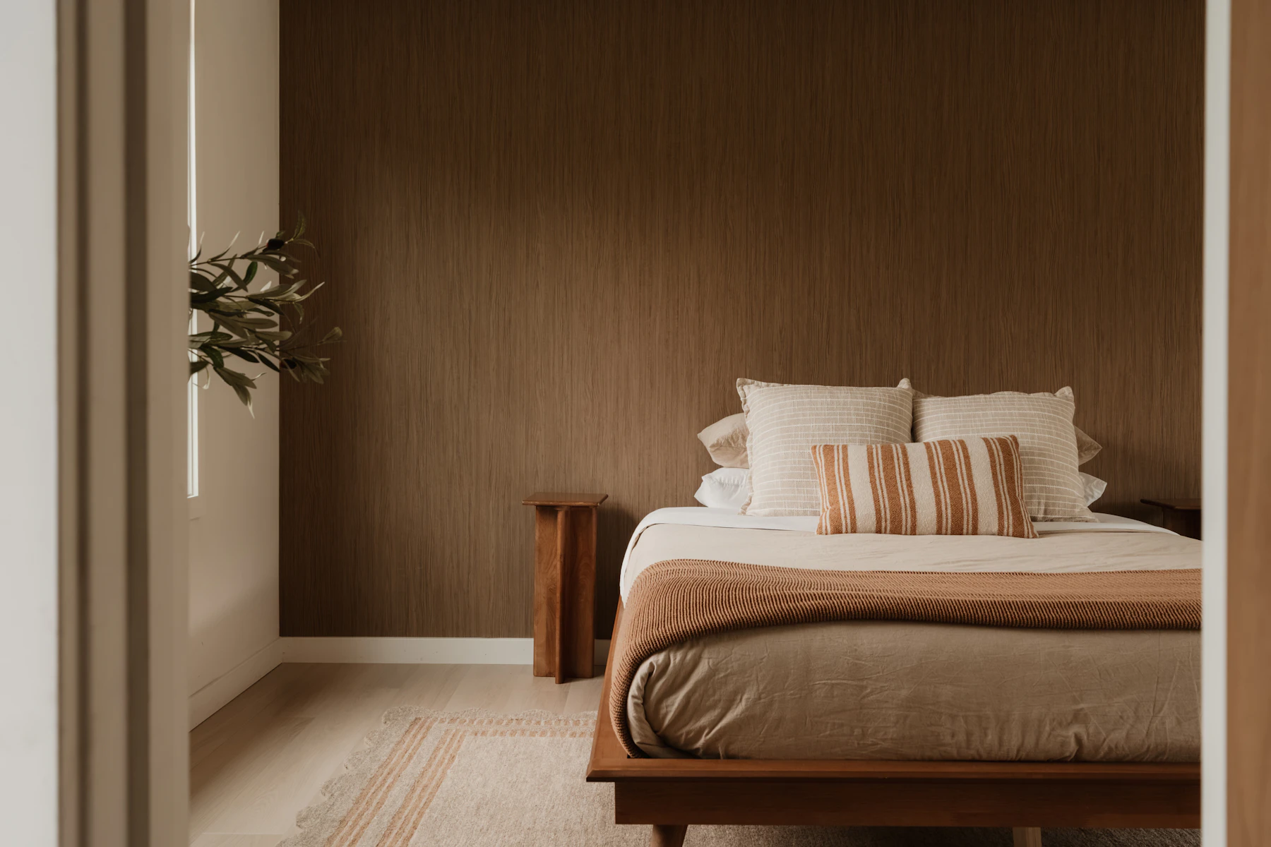 Warm modern bedroom with bed, pillows, wood furniture, and natural light