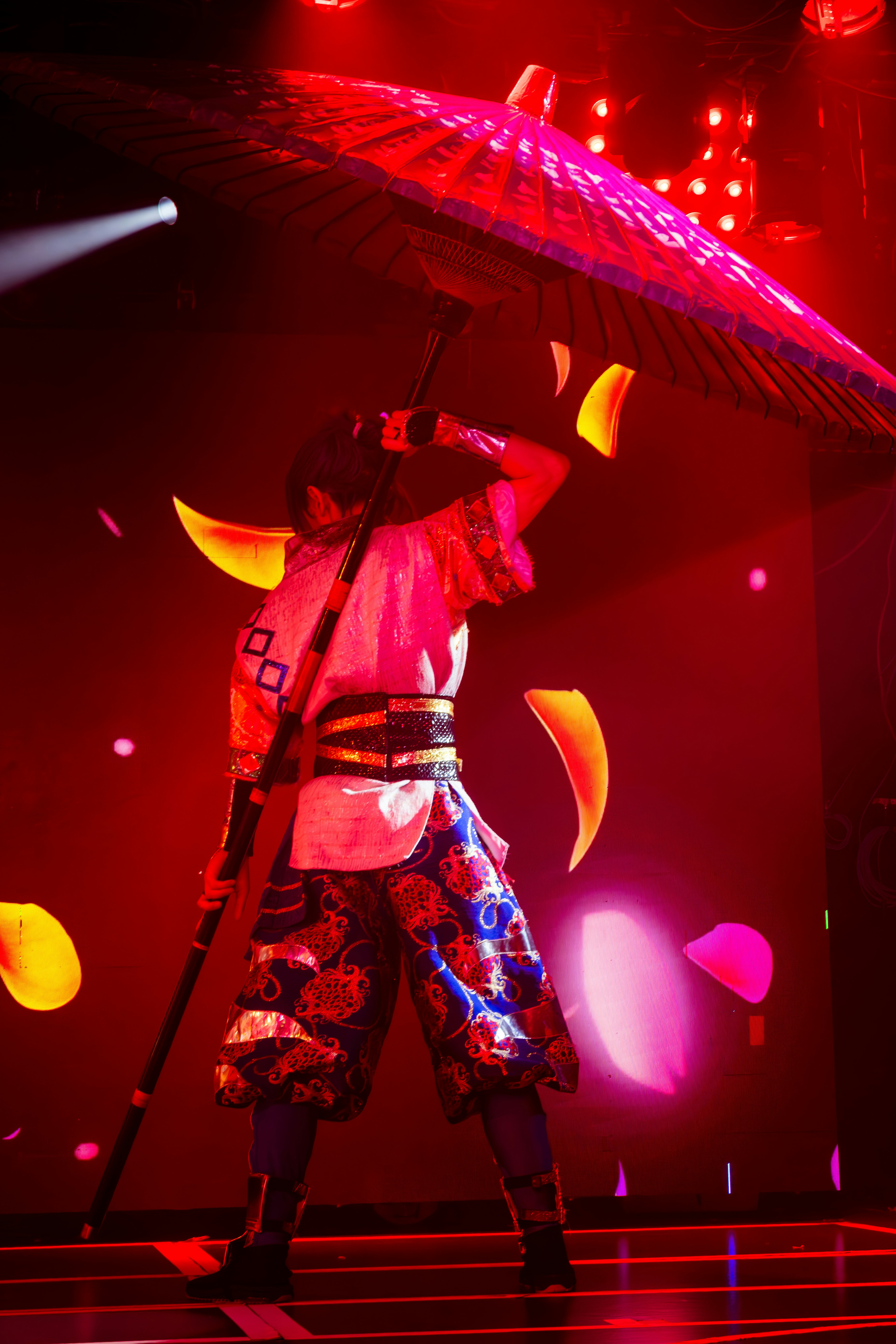 A person in traditional costume holding a red parasol under bright red stage lights
