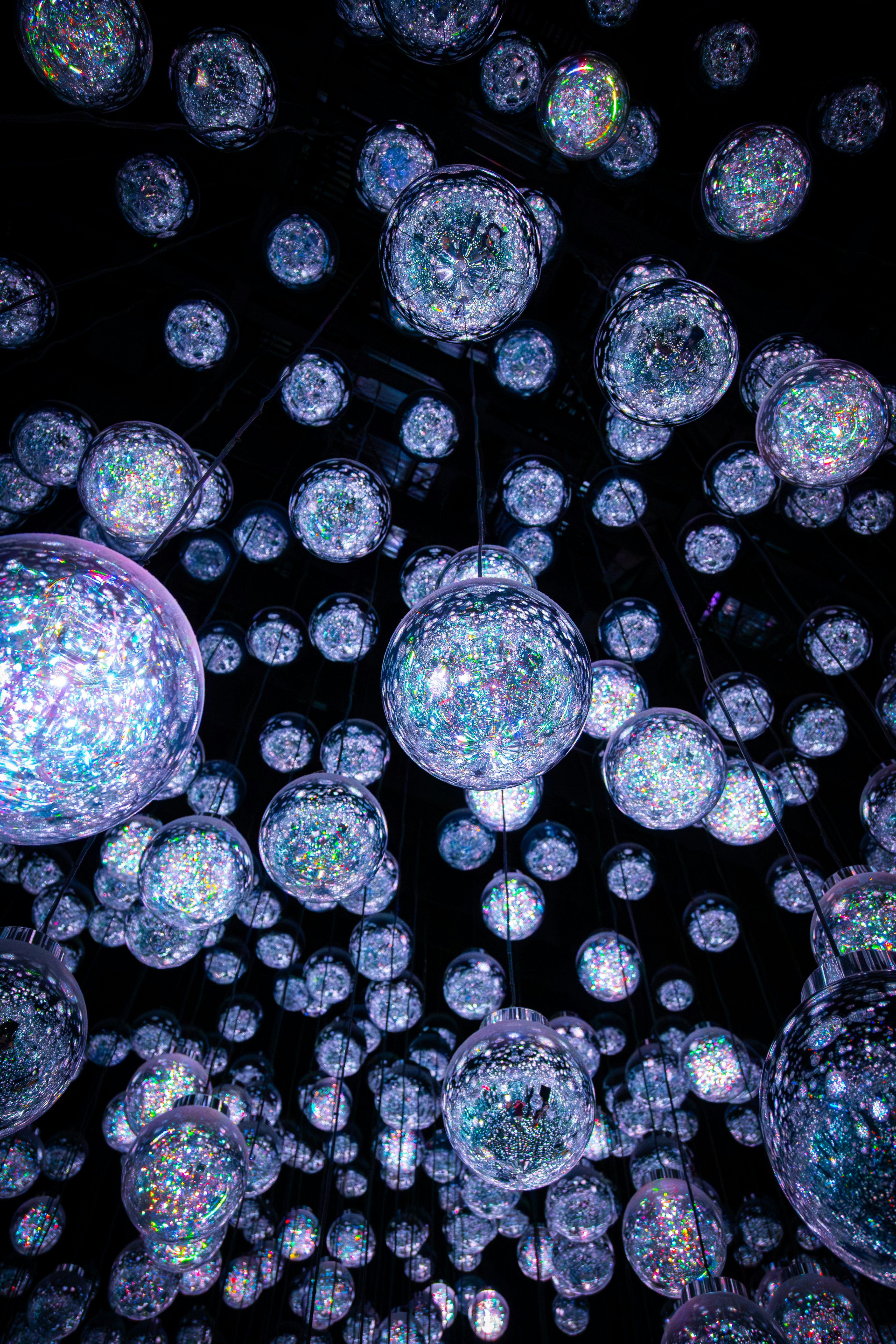 Molte sfere di vetro luminose con glitter iridescenti sospese su uno sfondo scuro