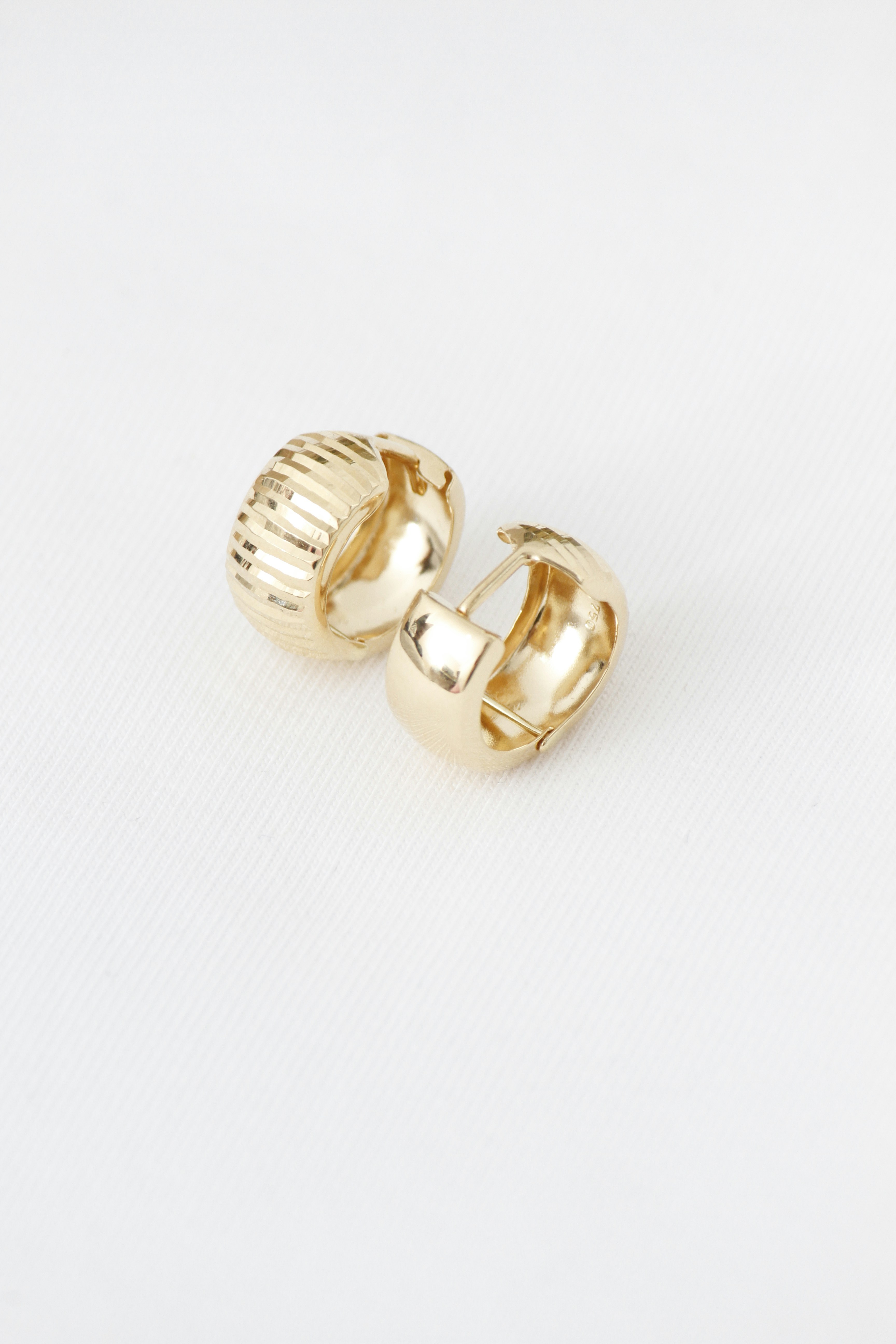 Two gold hoop earrings, one ribbed, on white background.