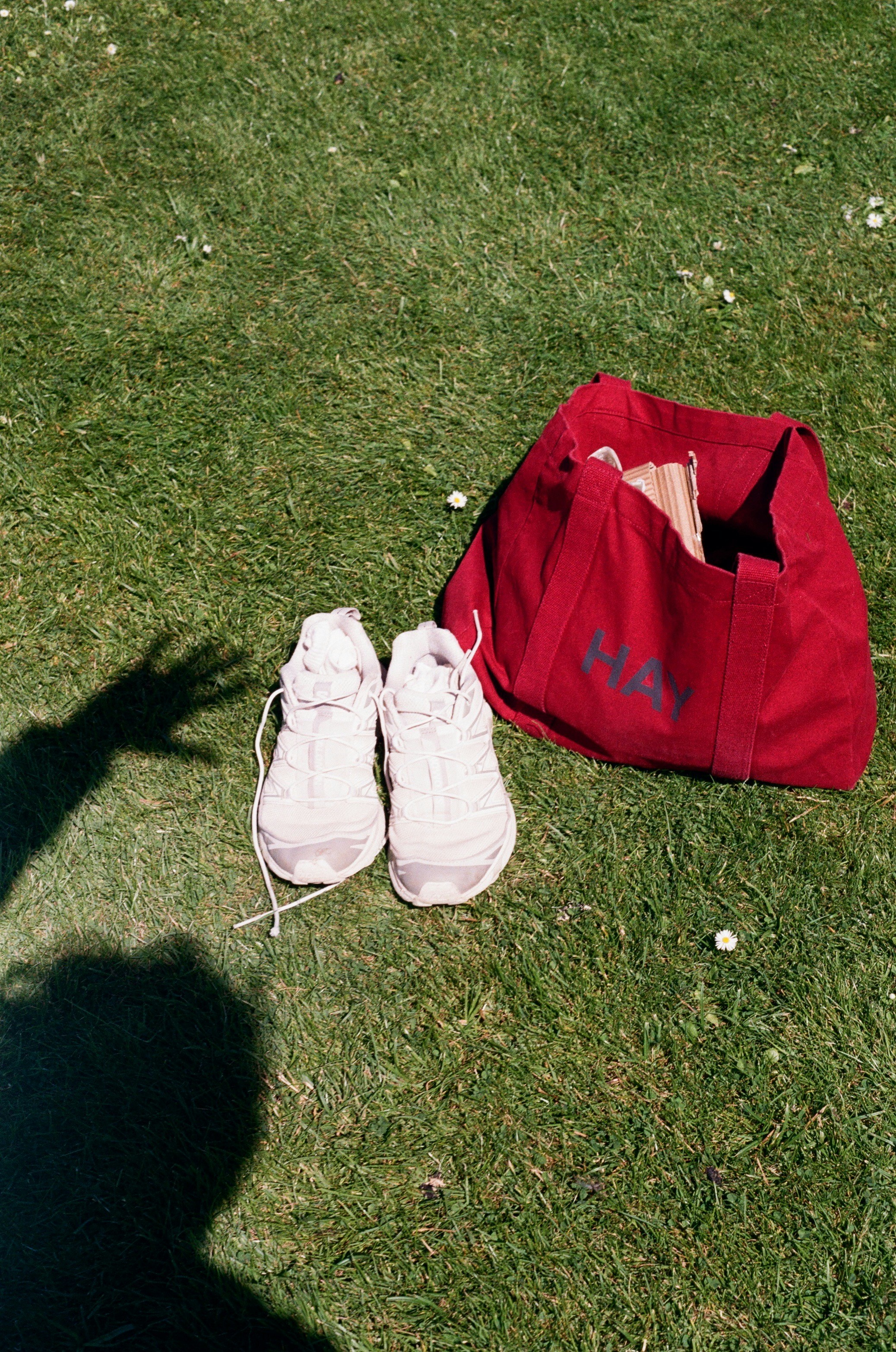 White sneakers and a red tote bag on green grass.