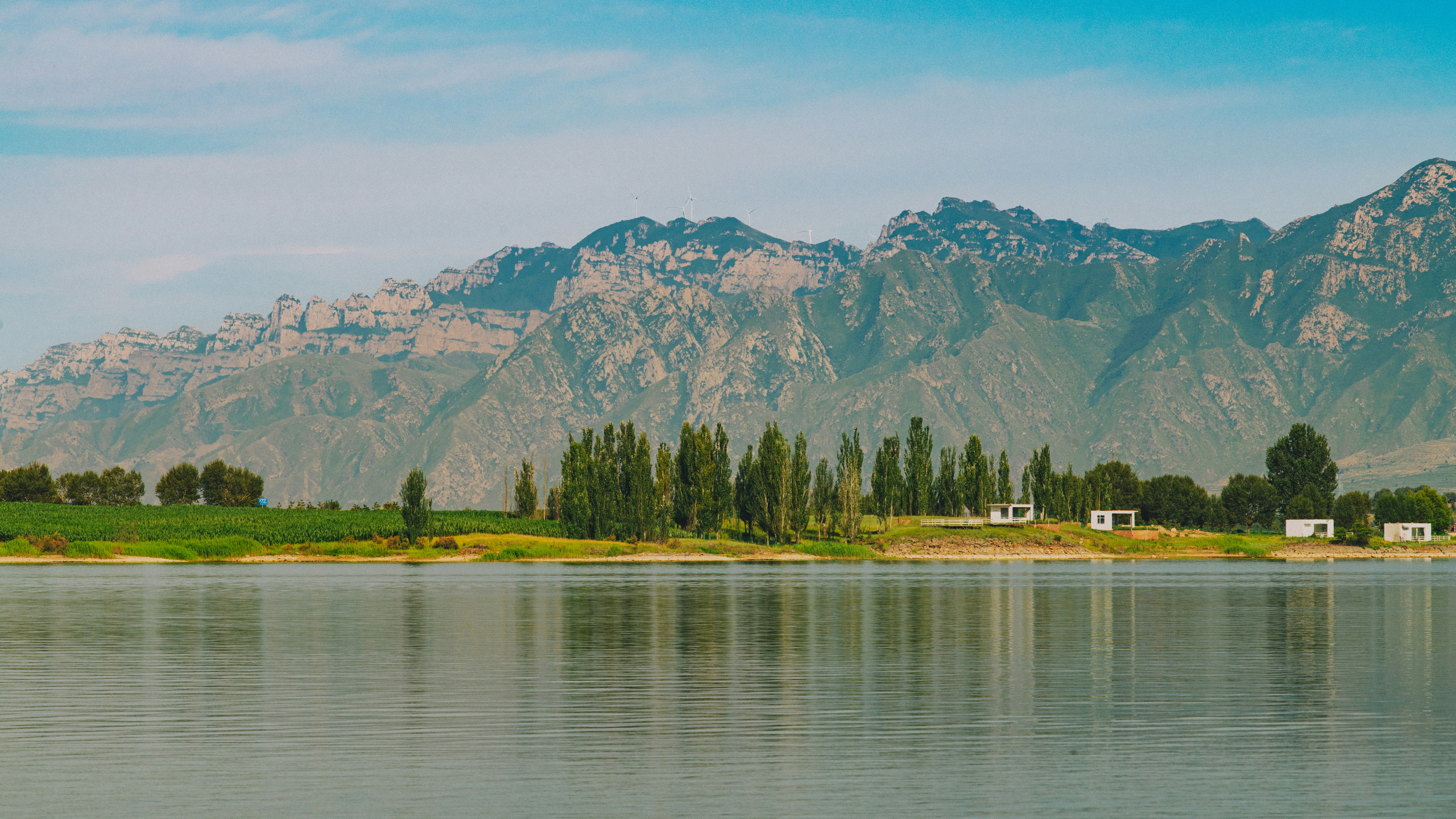 Lago sereno, alberi verdi, piccoli edifici e montagne maestose.