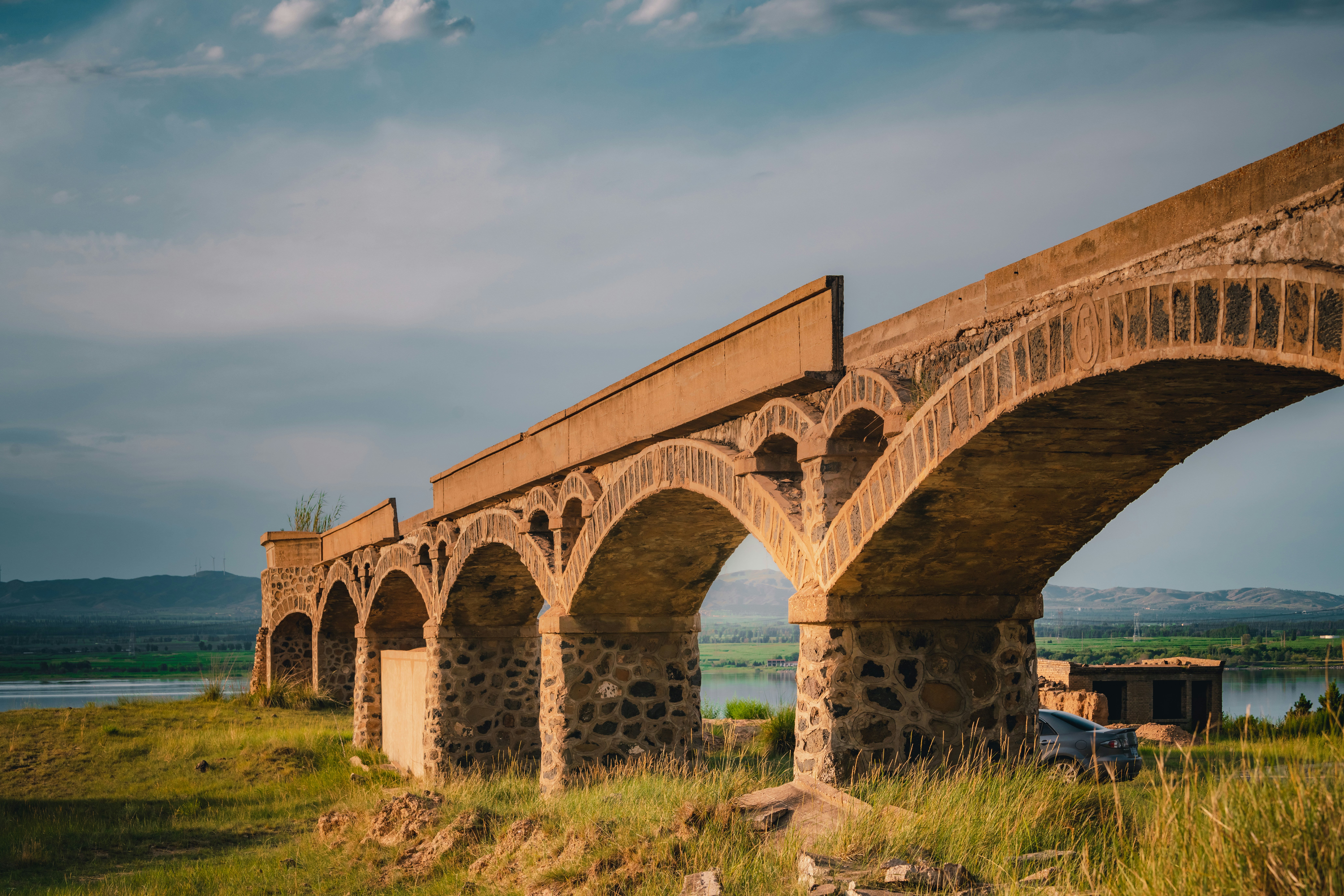 Storico ponte ad arco in pietra su un paesaggio erboso al tramonto.