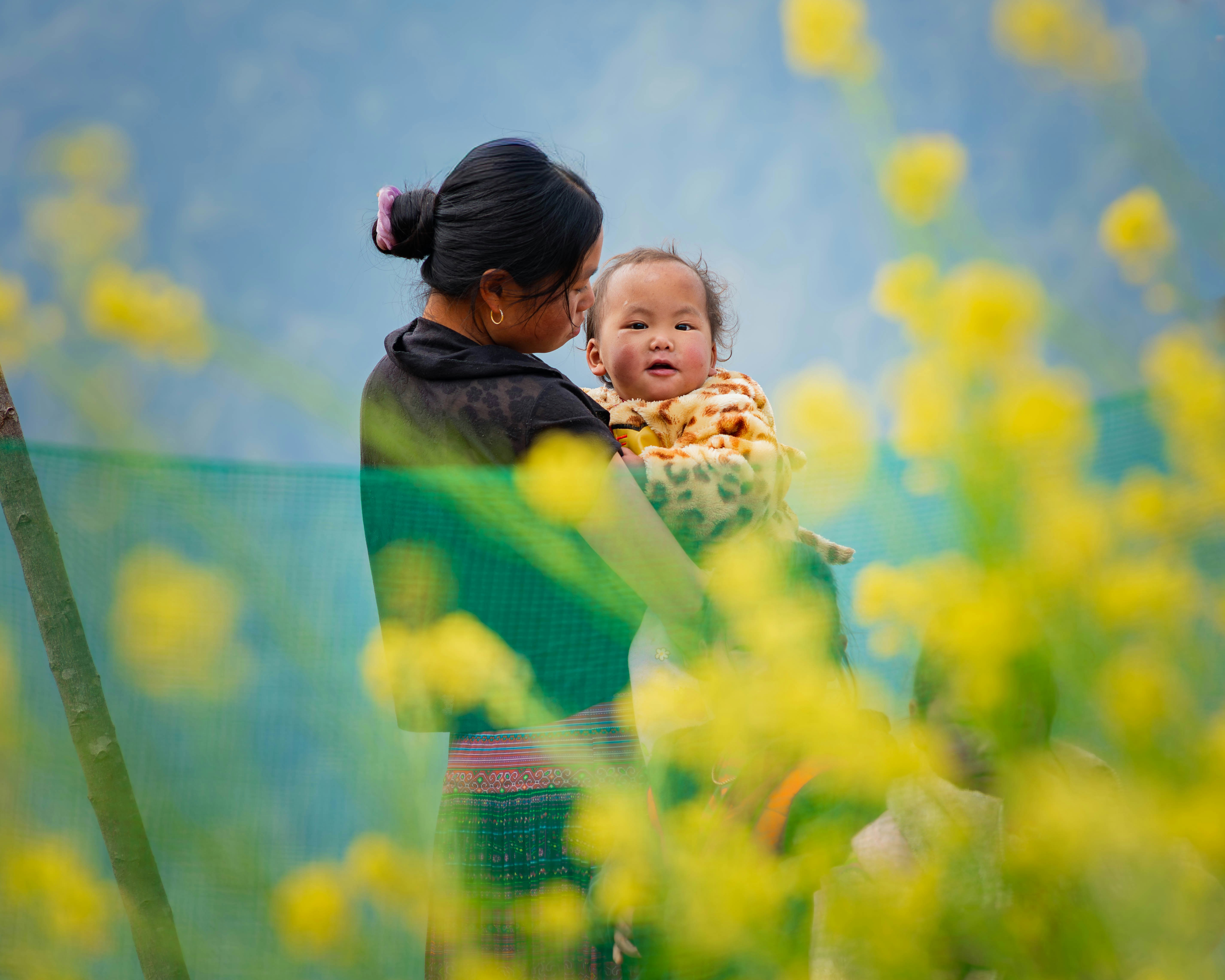 Mother holding her smiling baby, surrounded by bright yellow flowers