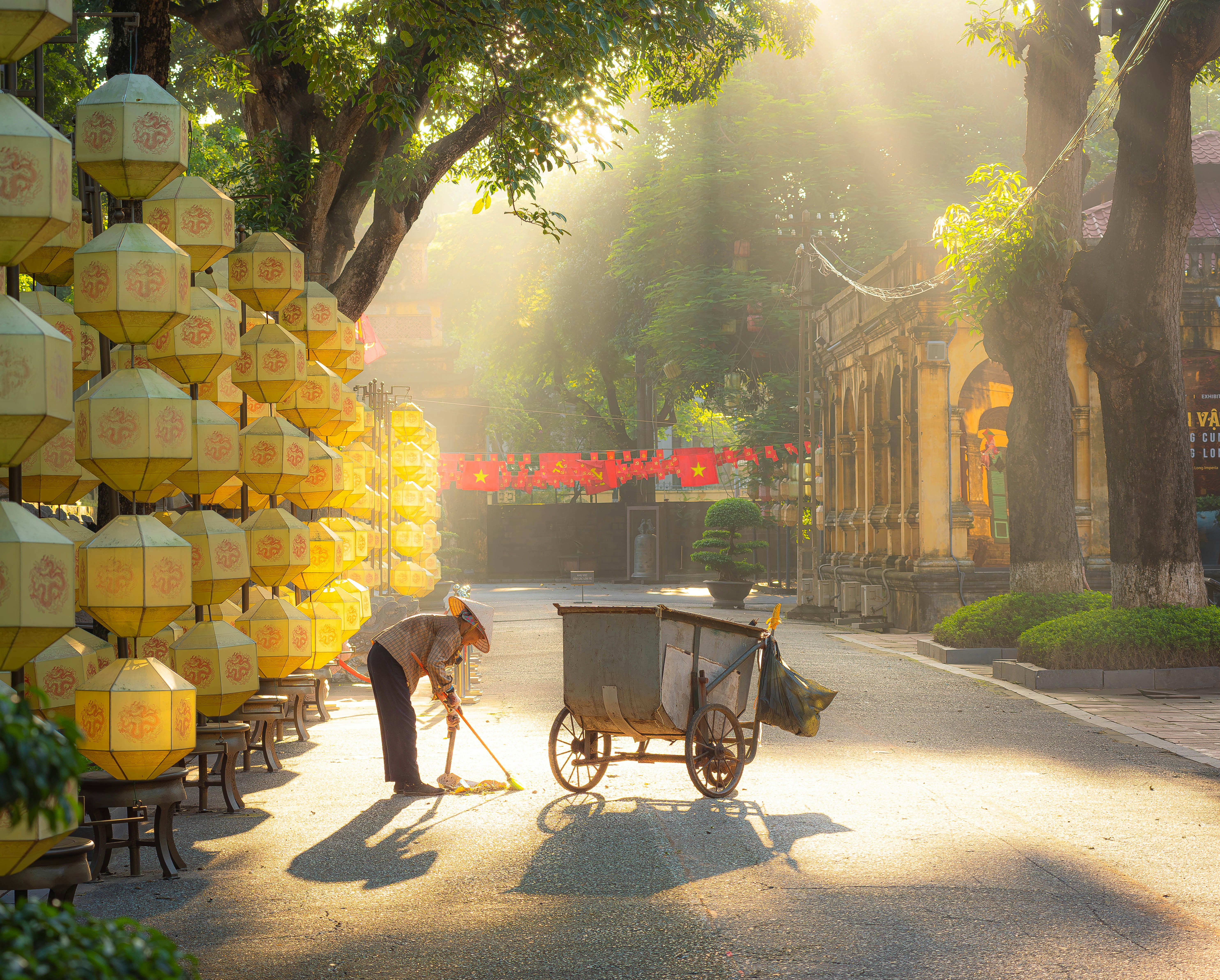 Street sweeper works amidst glowing lanterns and sunbeams