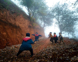 Children run and jump on a misty, leaf-covered dirt road.