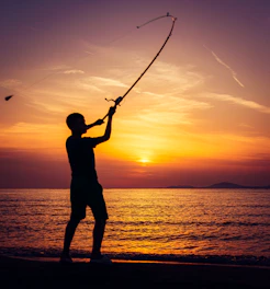 Silhouette of a person fishing at sunset by the ocean