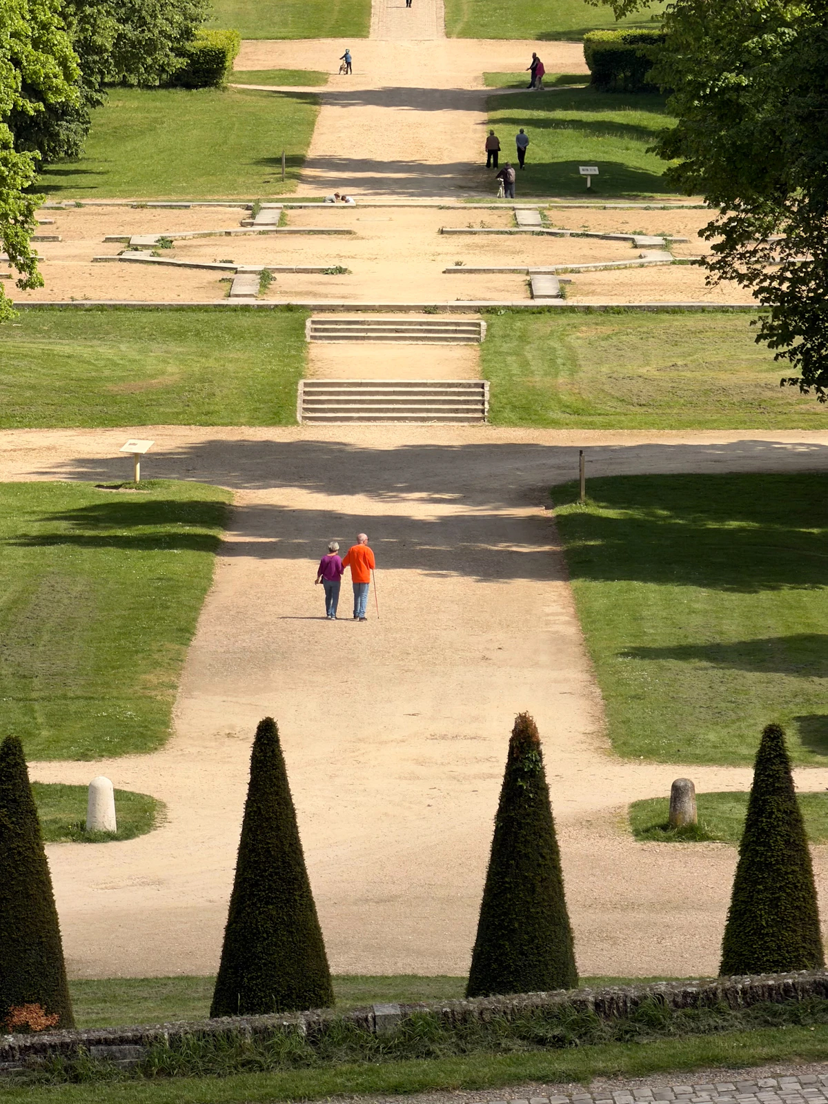 People walking along a formal garden path with steps and fountains.
