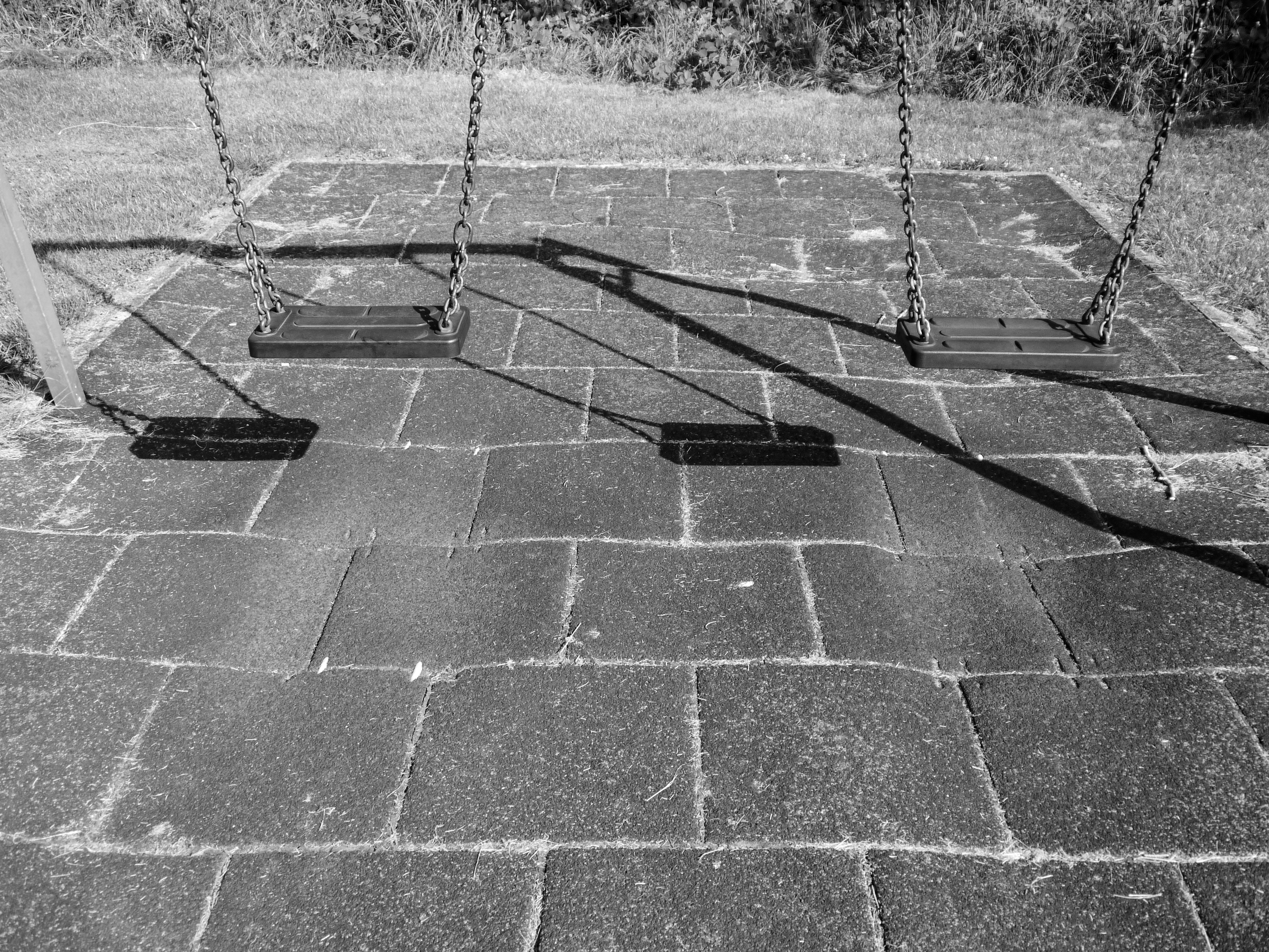 Three empty swings on a paved playground surface.