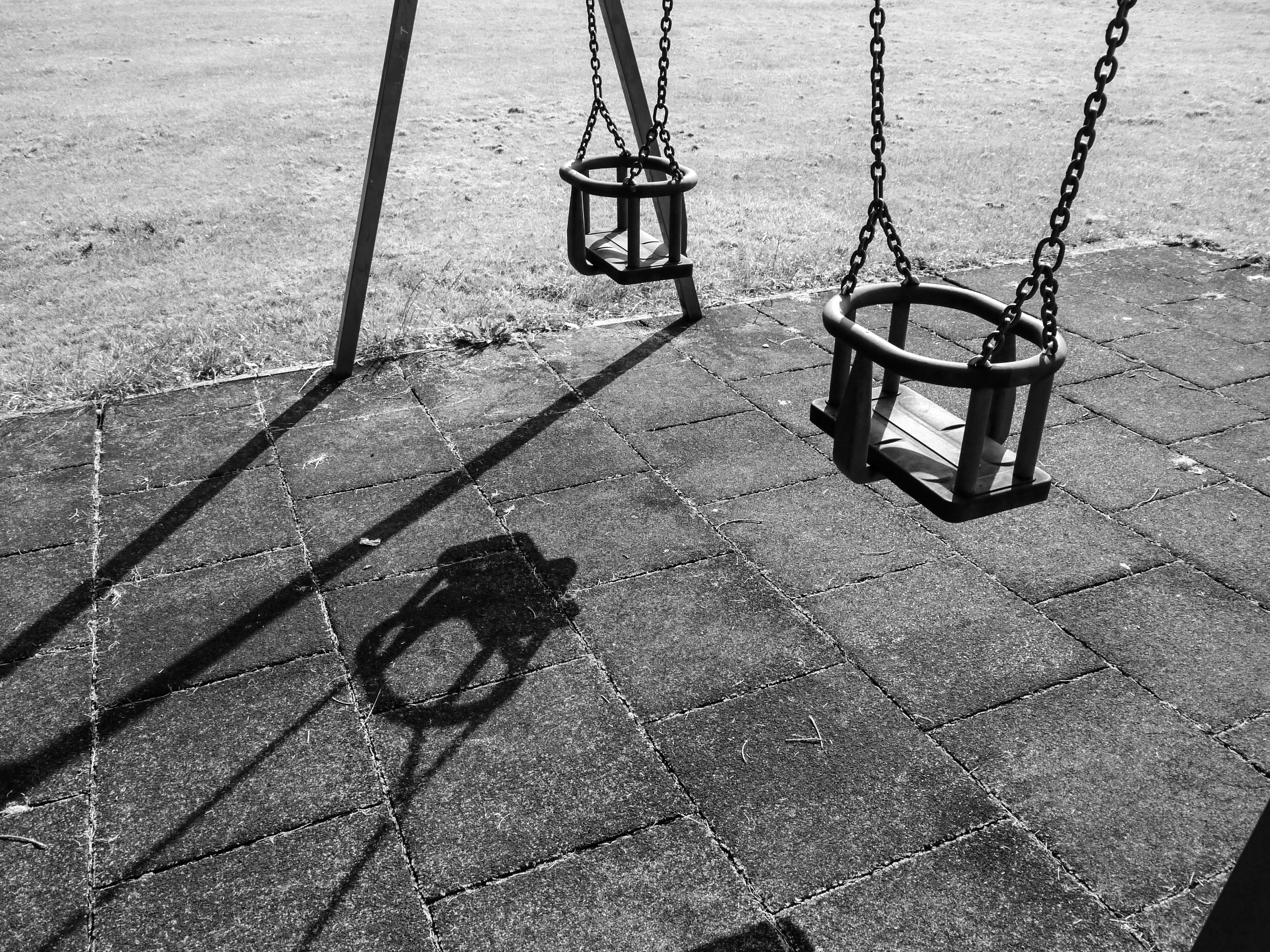 Empty baby swings with long shadows on a playground.