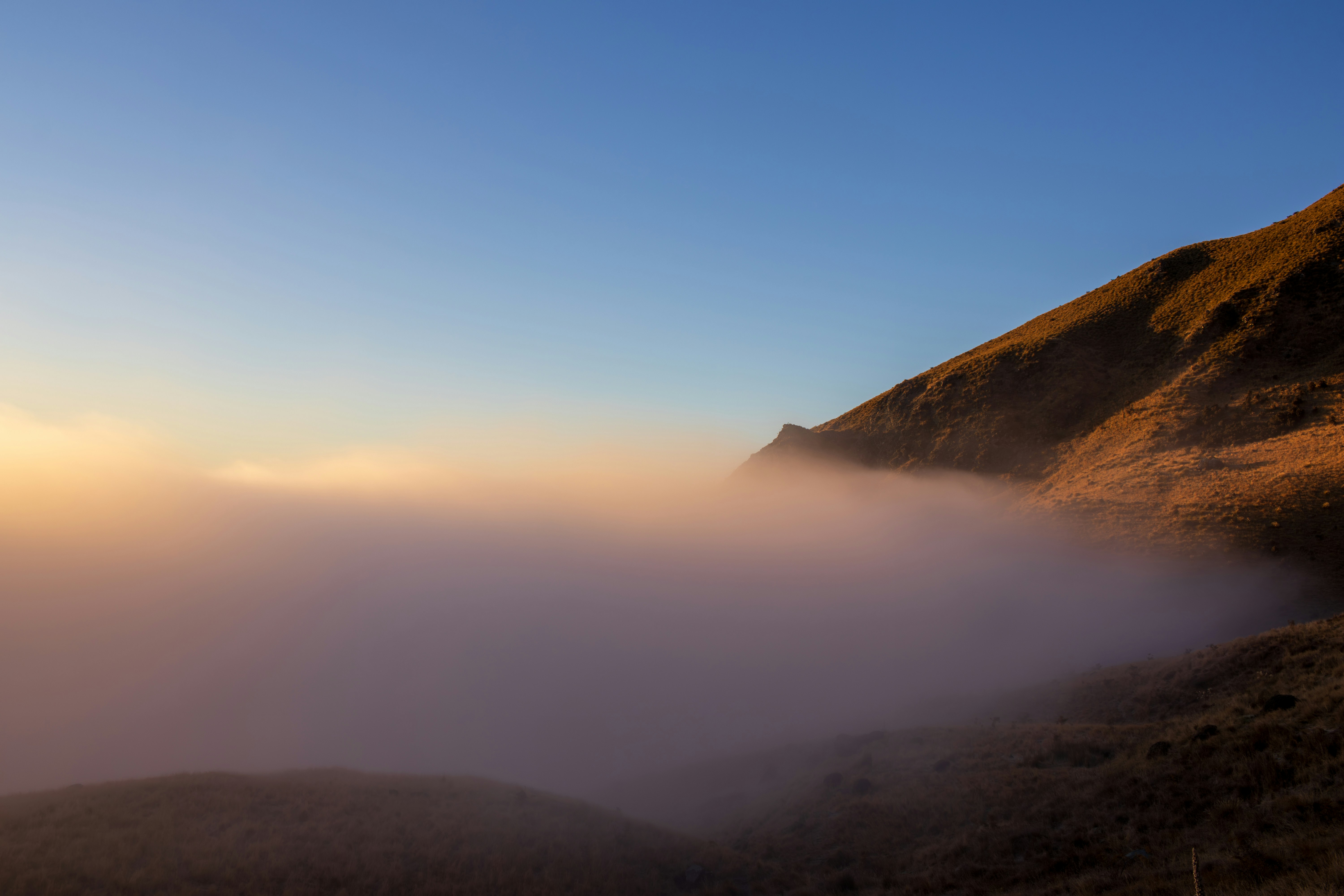 Golden light and fog partially obscure a mountain.